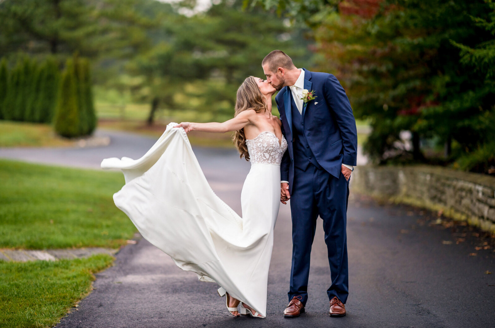 bride and groom, holding hands and kissing with the bride, holding the train of her wedding gown in the air after their wedding ceremony at Scotland run country club
