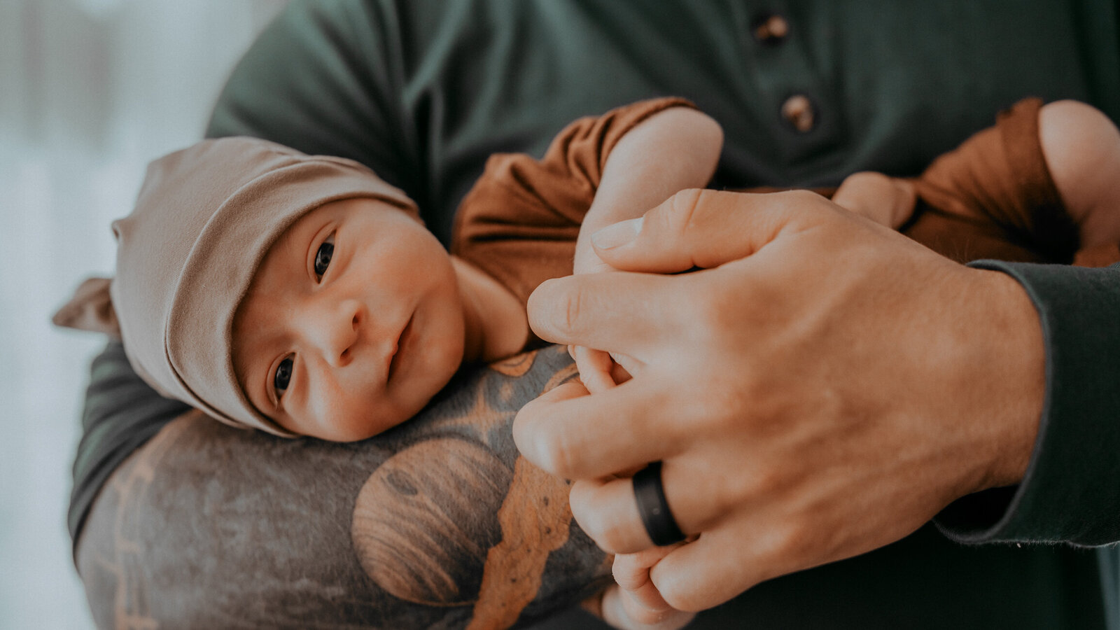 baby boy looks at camera laying in dad's tattooed arm