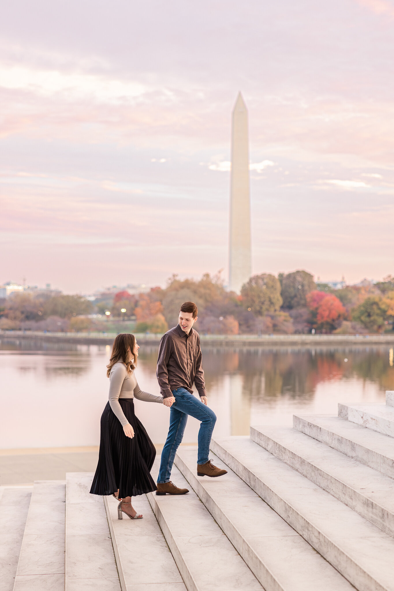 A man leads a woman up the steps of the Jefferson Memorial with Washington Monument in background