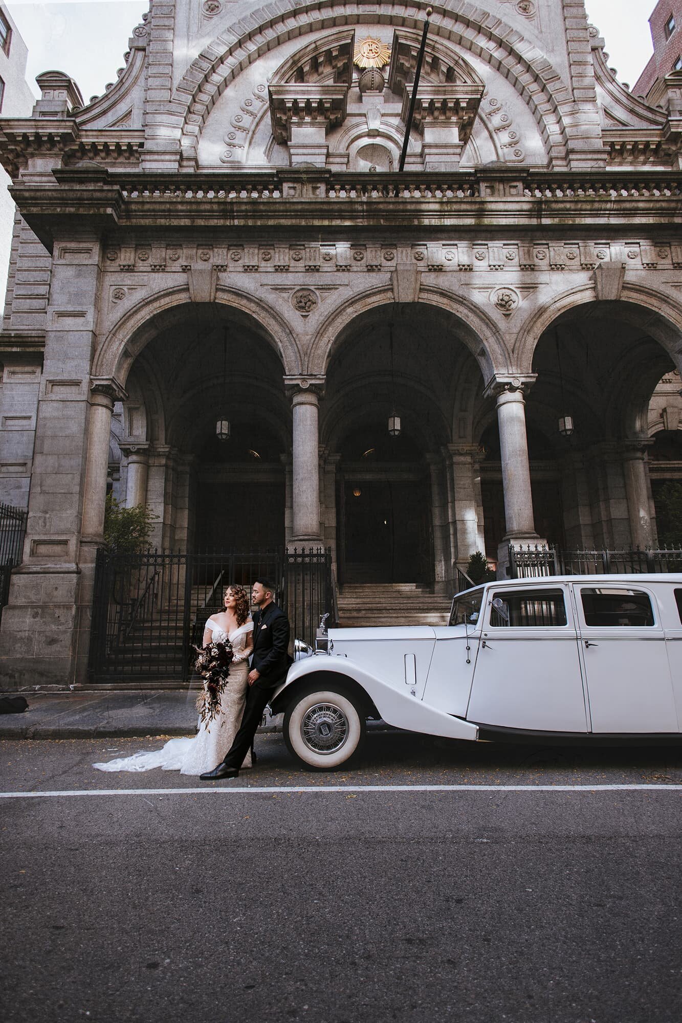 Editorial-style wedding portrait outside The Church of St. Francis Xavier in New York City, featuring a bride and groom with a vintage white car, captured by Logrono & Co. Weddings.