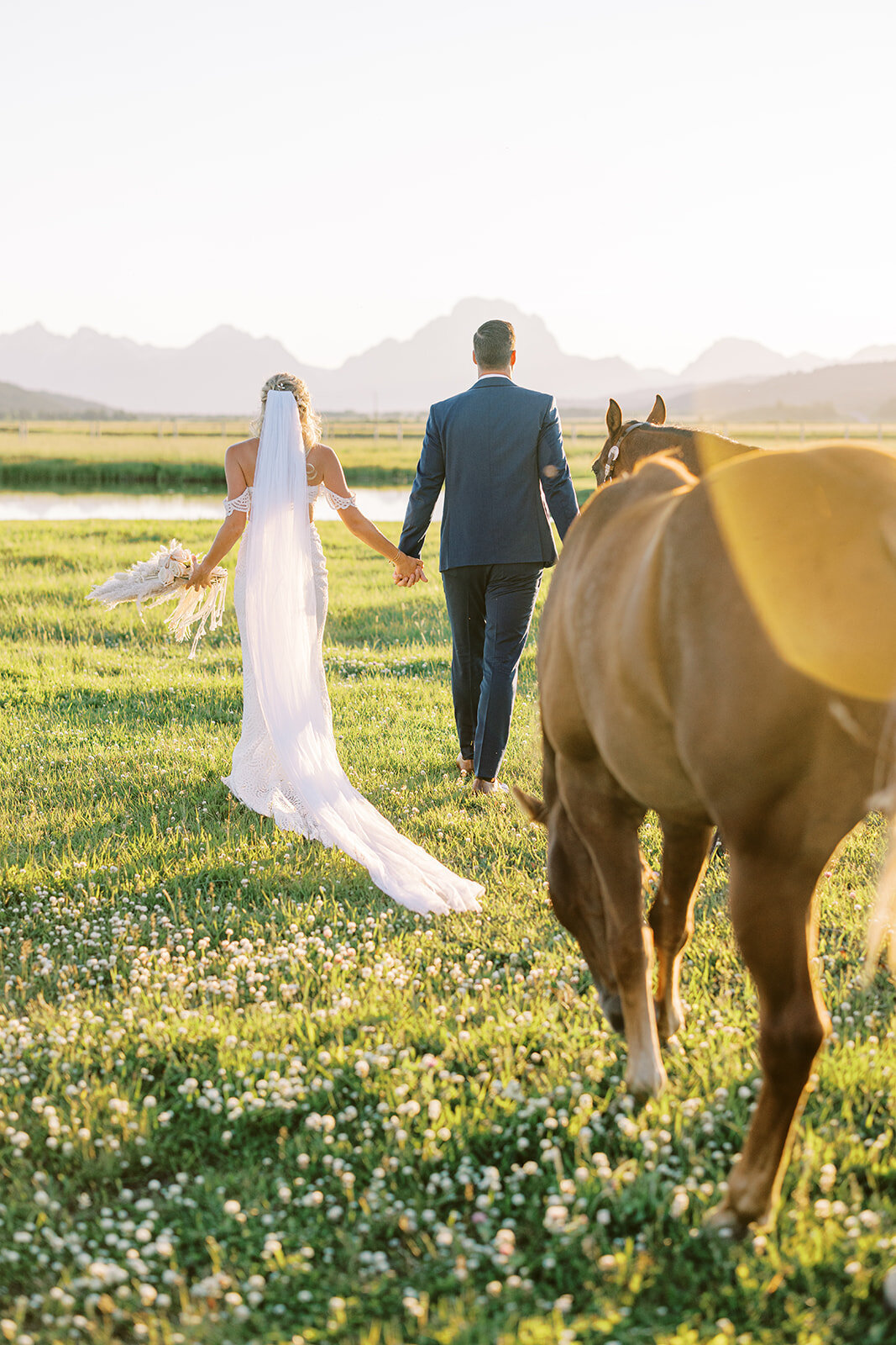 Bride and groom stroll with a horse in front of a lake and the Teton mountain range after their wedding at Diamond Cross Ranch