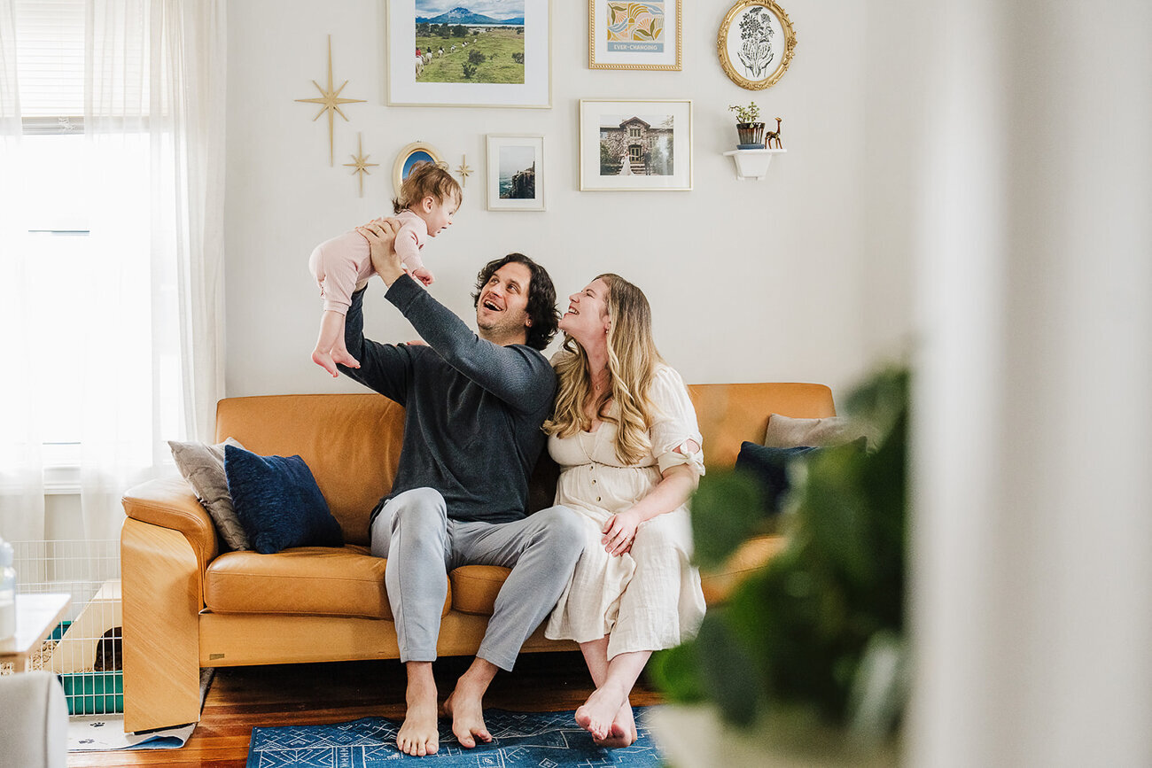 parents lift baby in air in living room in front of gallery wall