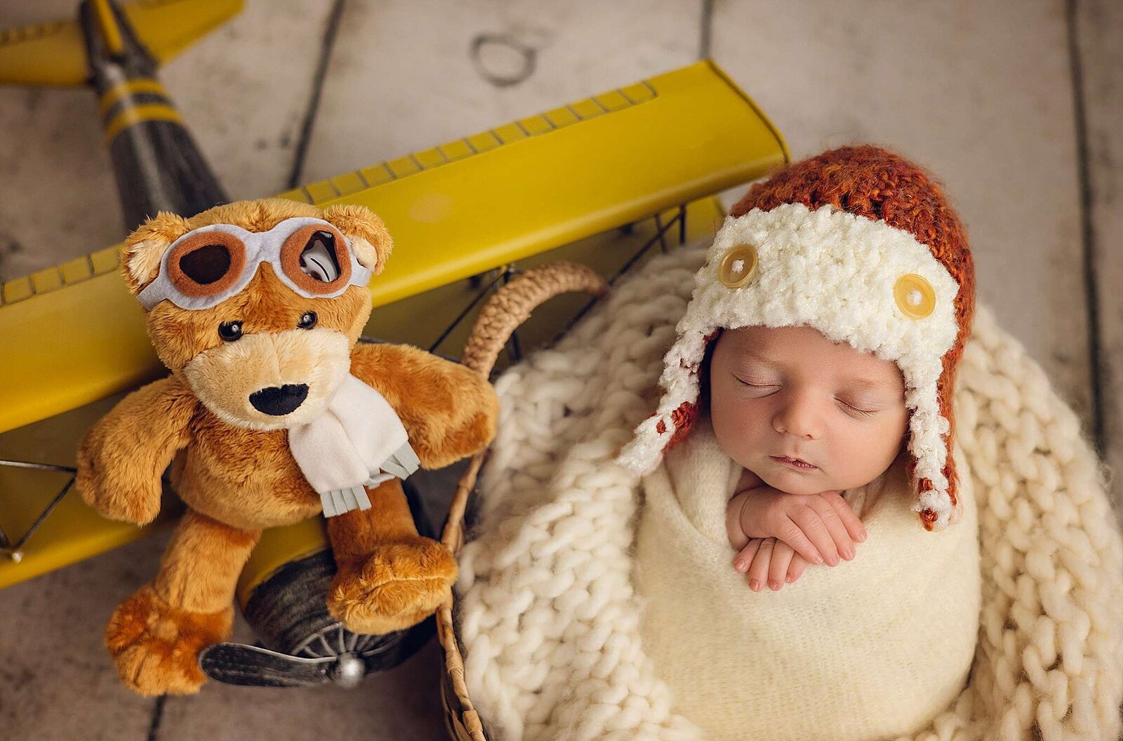 A peaceful newborn boy wearing a cute aviator hat, sleeping next to an aviator teddy bear, captured by Bia Schaefer, Orlando's expert newborn photographer.