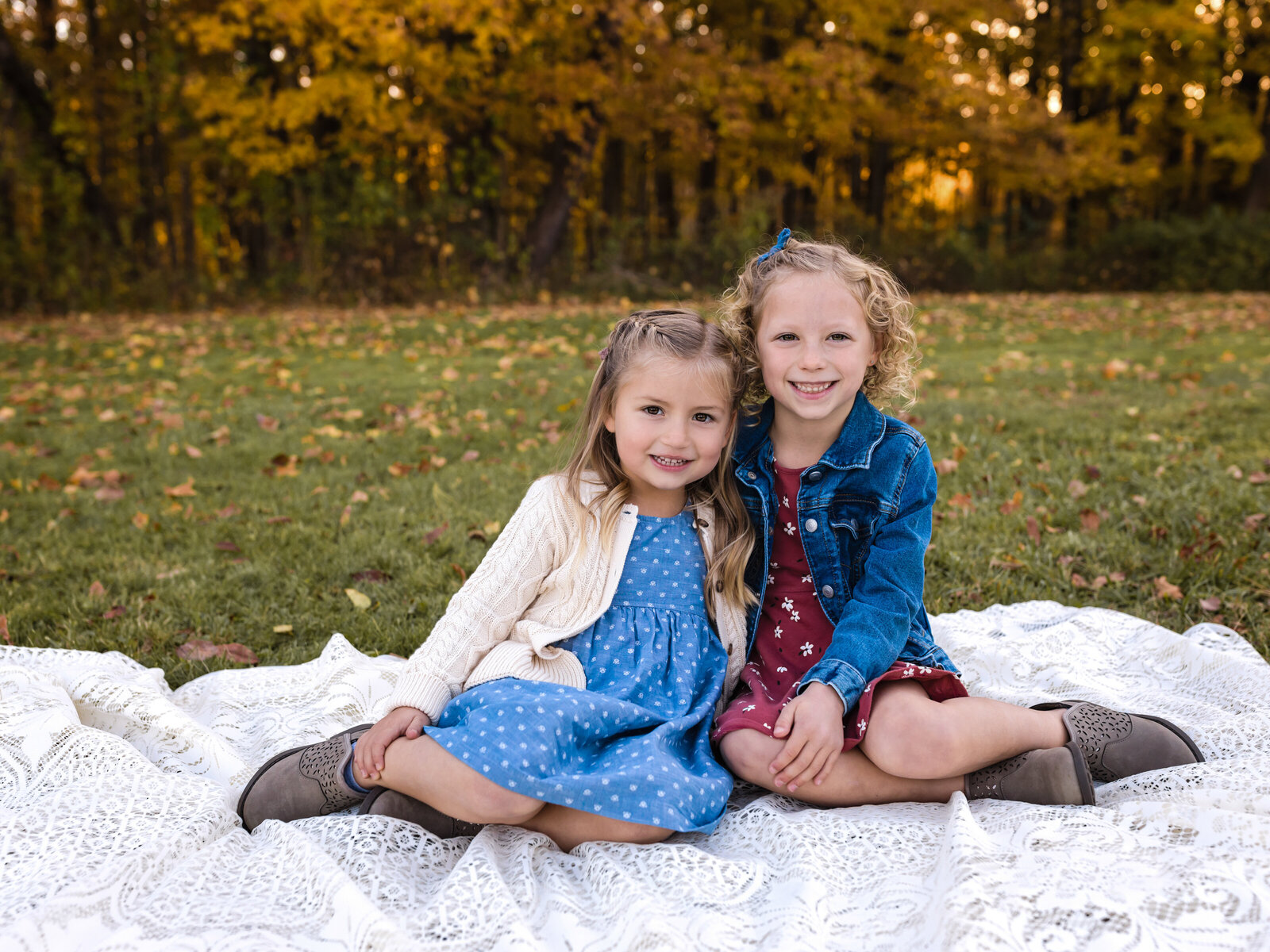sisters sitting on white lace blanket for fall family photos at brecksville reservation in cleveland ohio