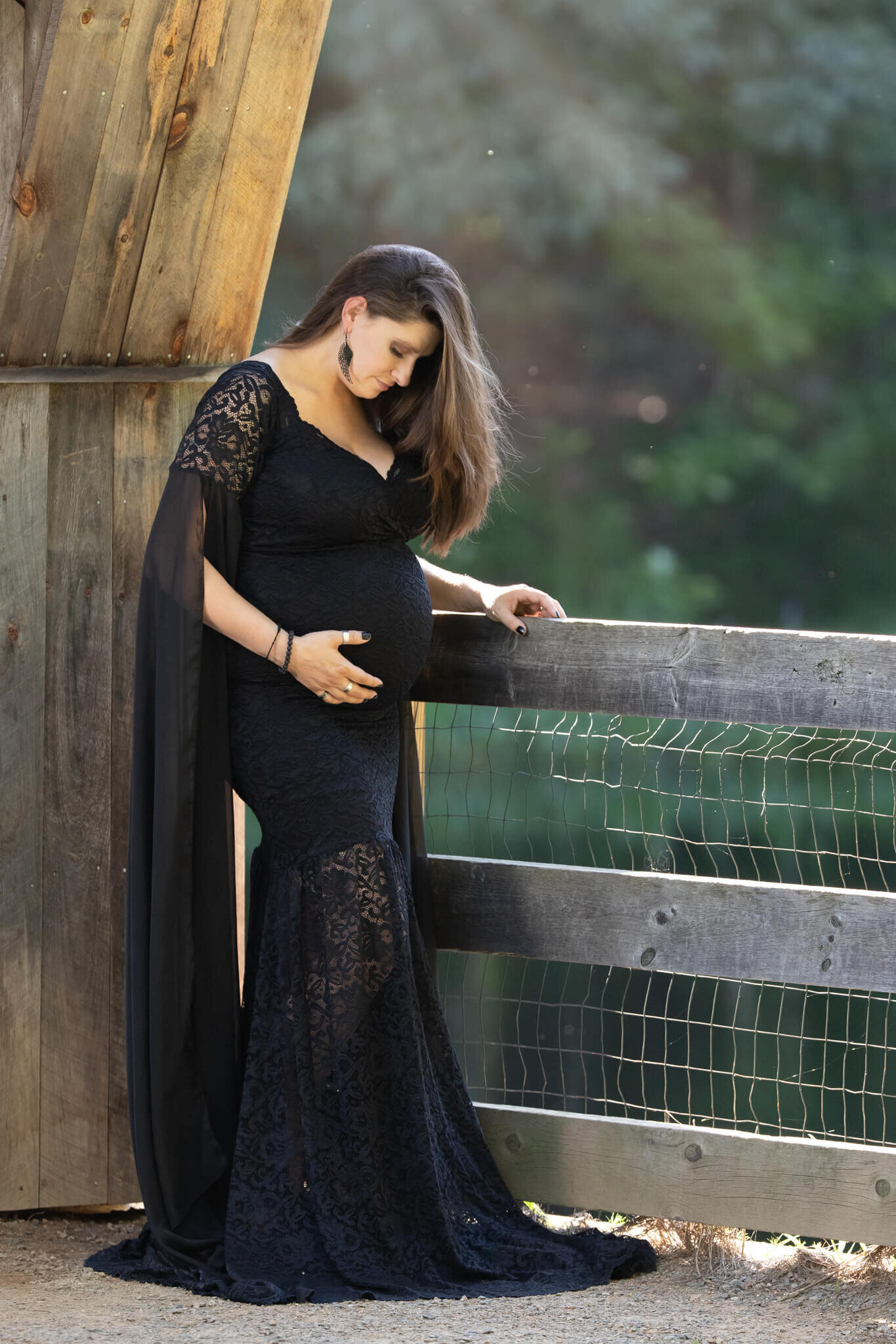 Maternity photography of mother in long black gown holding her belly and looking down at her belly