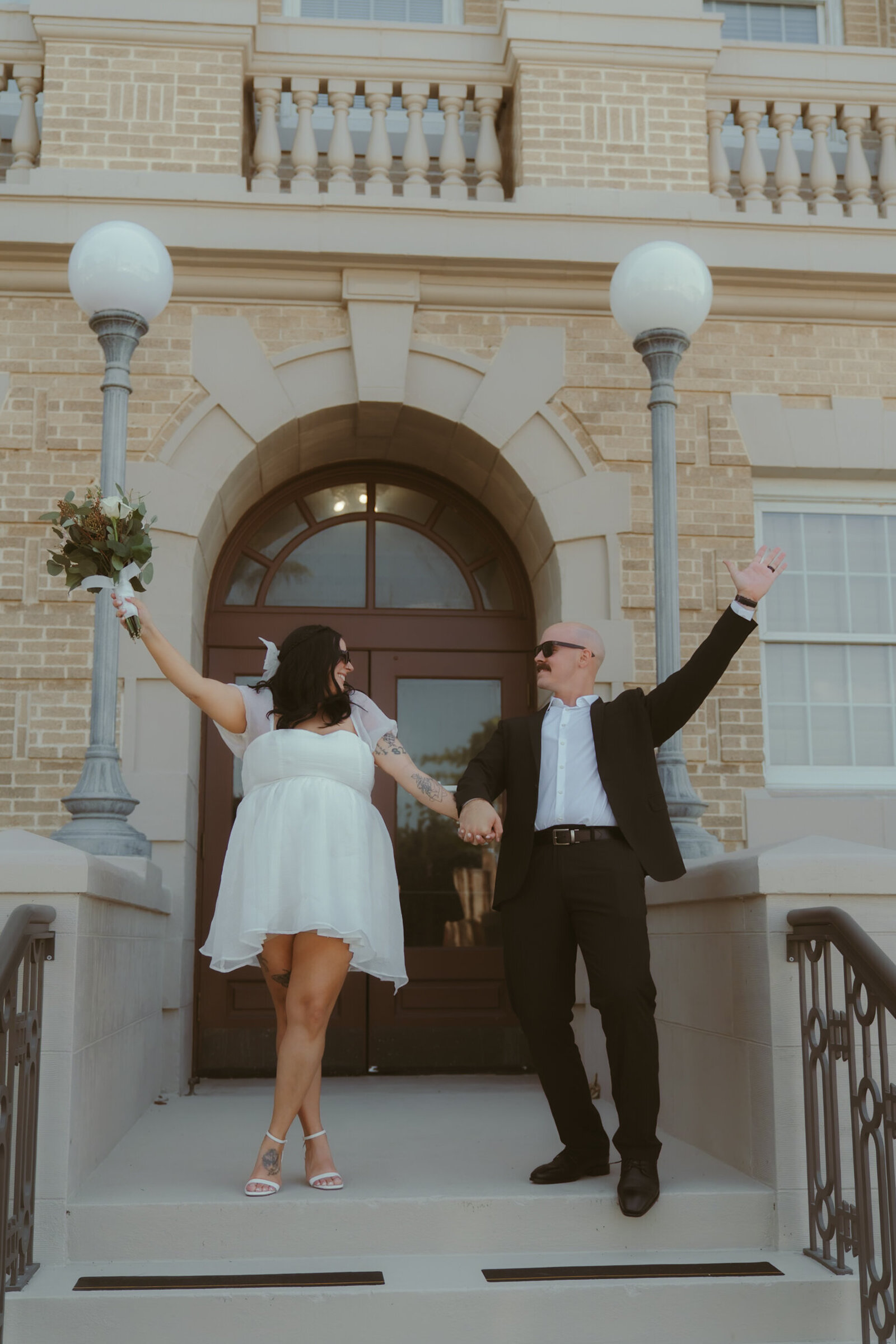 Fun courthouse wedding photo with the bride and groom raising their hands in celebration.