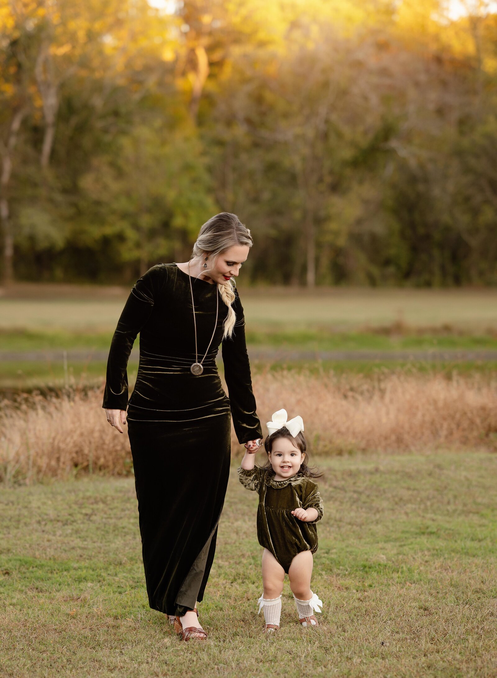 Mom holding little girls hands and walking in an open fall field.