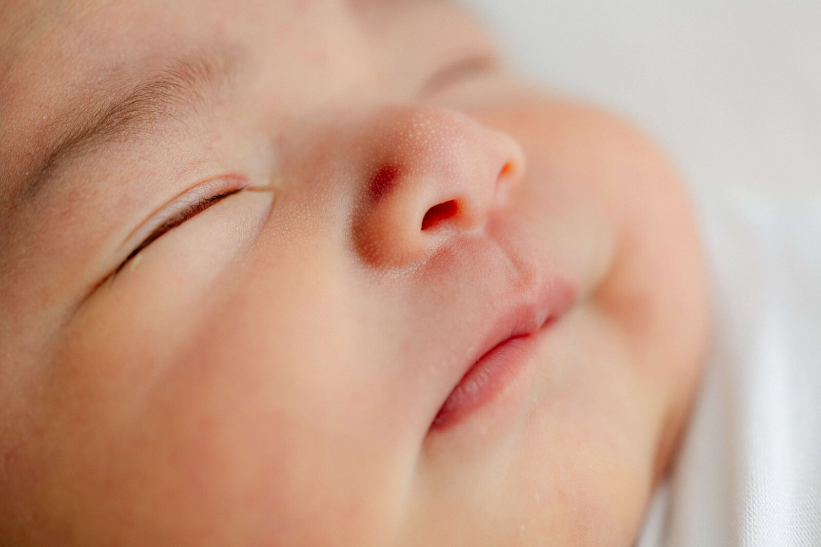 Baby peacefully sleeping, wrapped in a lace swaddle, on a textured blanket with neutral tones.