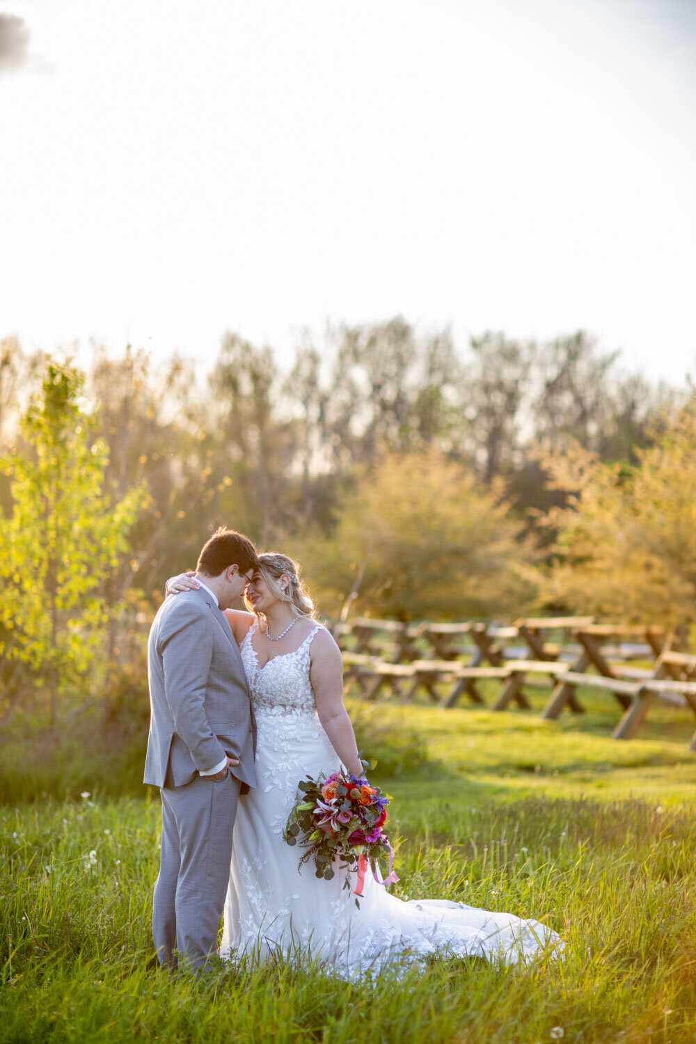 Bride and groom sharing a tender moment in a sunlit field with a colorful bouquet