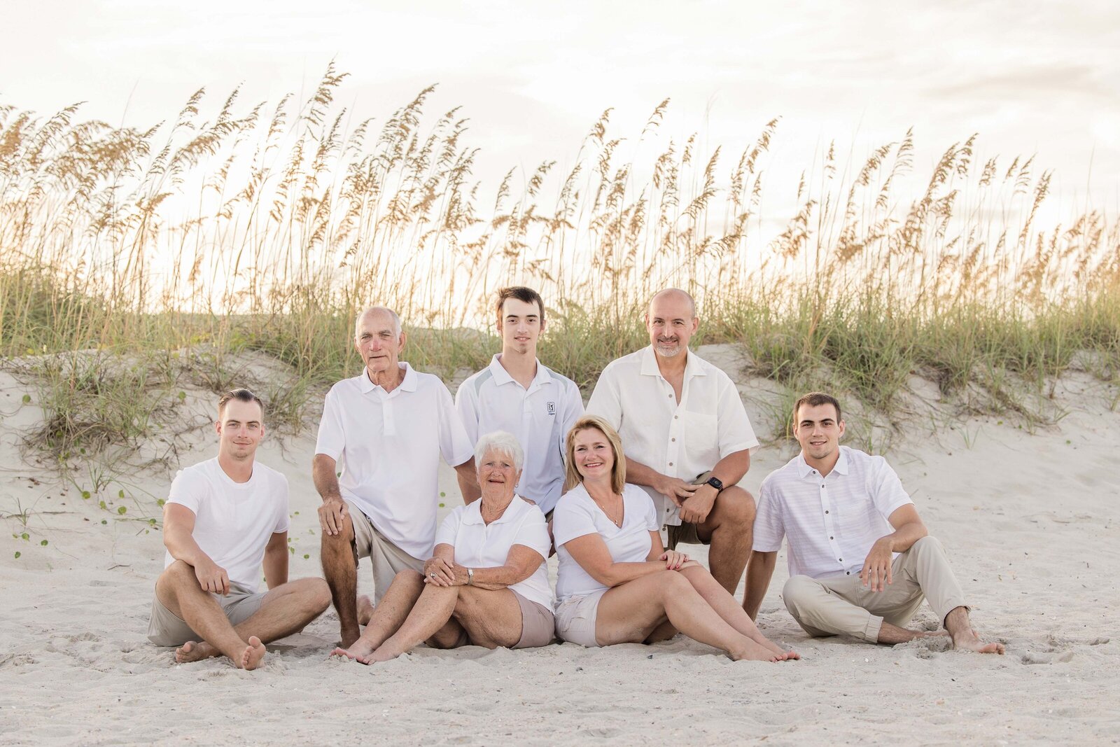 A family sits together on sandy dunes, surrounded by swaying sea oats. Dressed in white, they capture a serene and timeless beach setting. Perfect for artistic family photography in Wilmington, NC, highlighting intimate family connections.