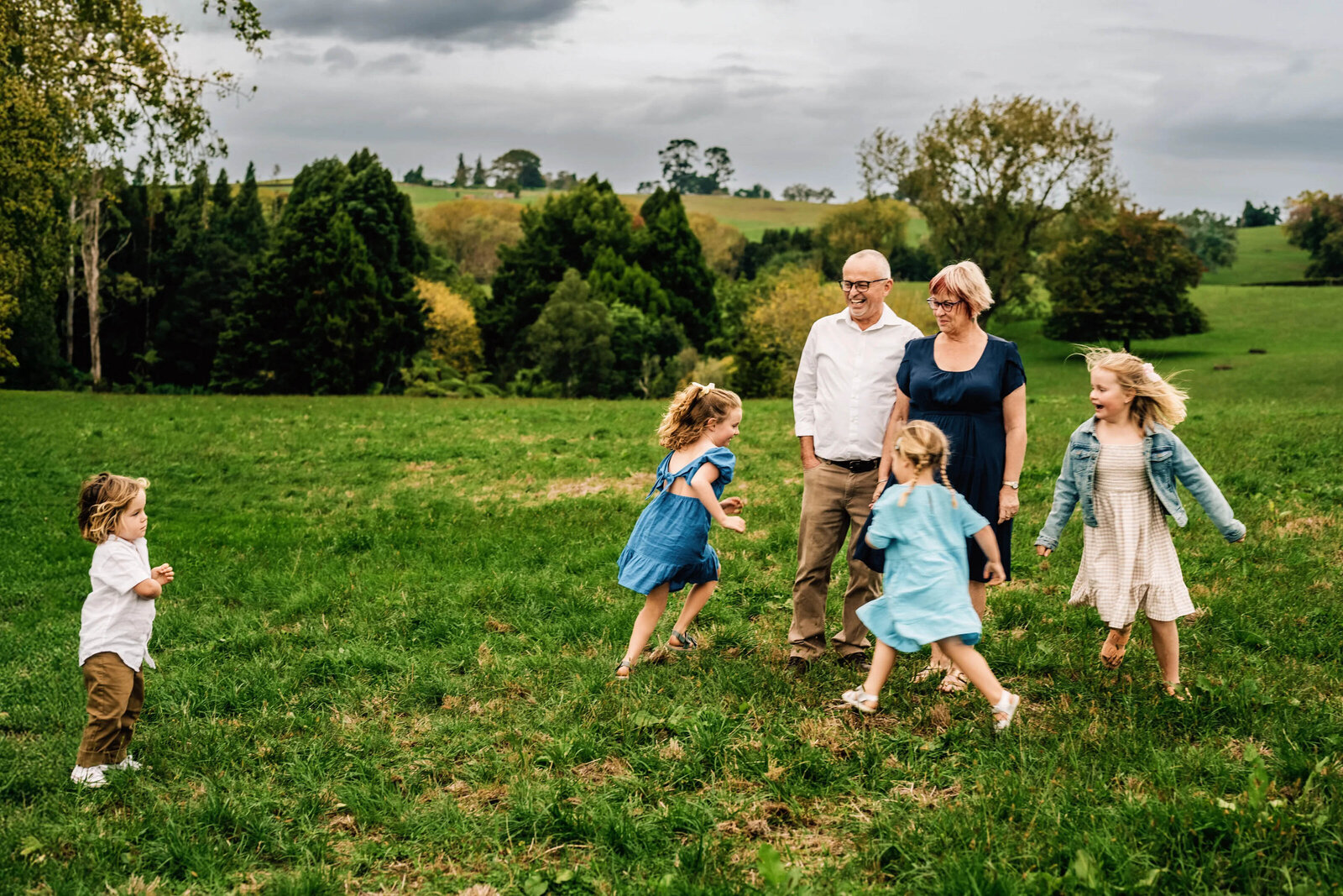 little grandchildren running around their gand parents with 1 boy just watching from afar