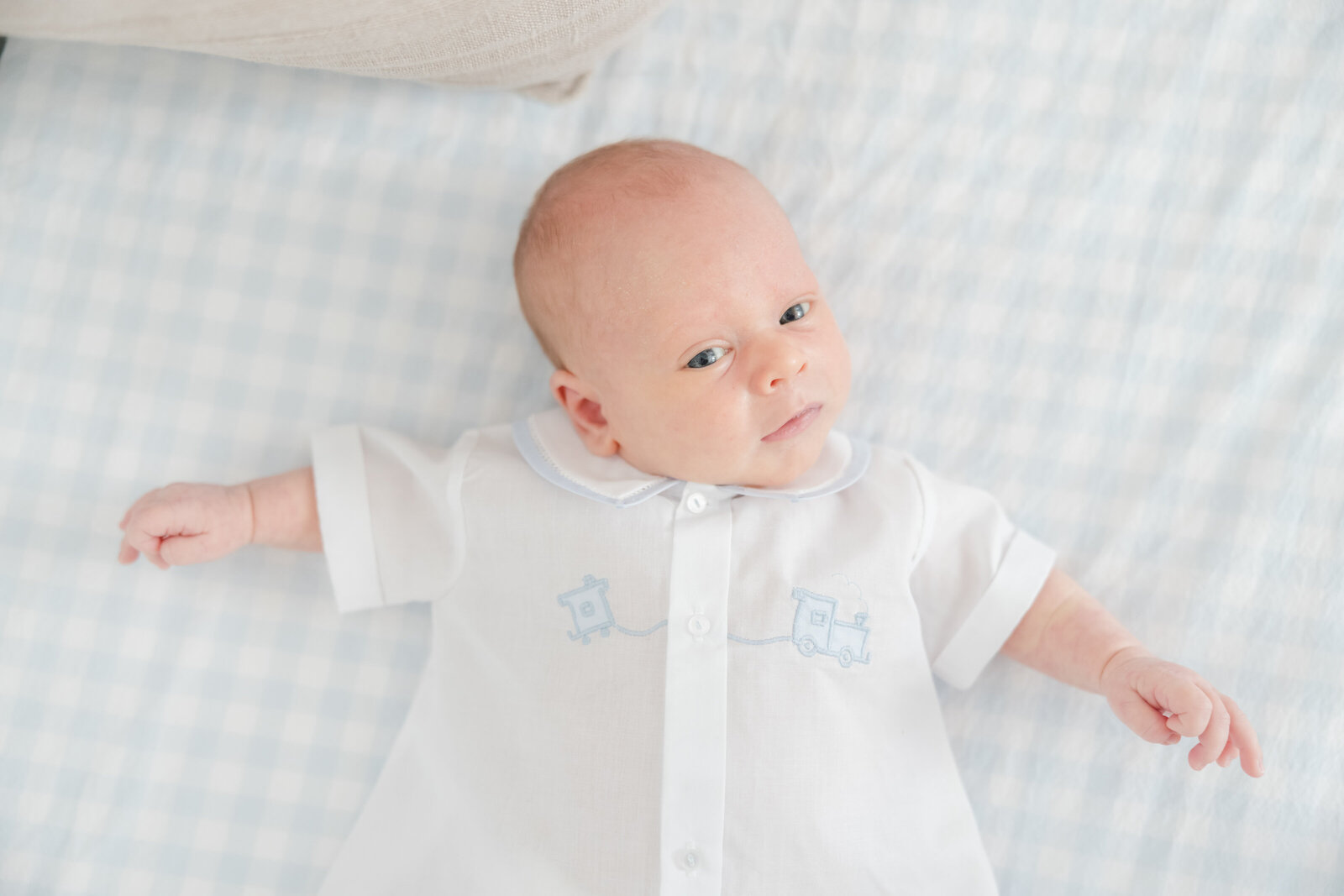 Baby boy laying on blue and white checkered crib sheet.