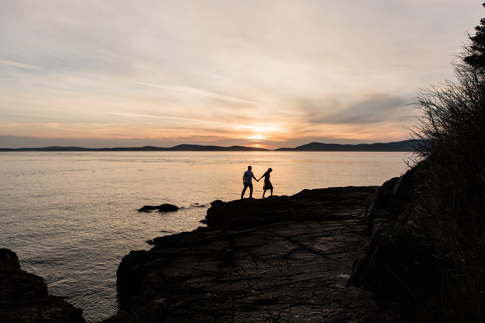 a woman leads her partner across a beach as the sun sets during their engagement session in anacortes
