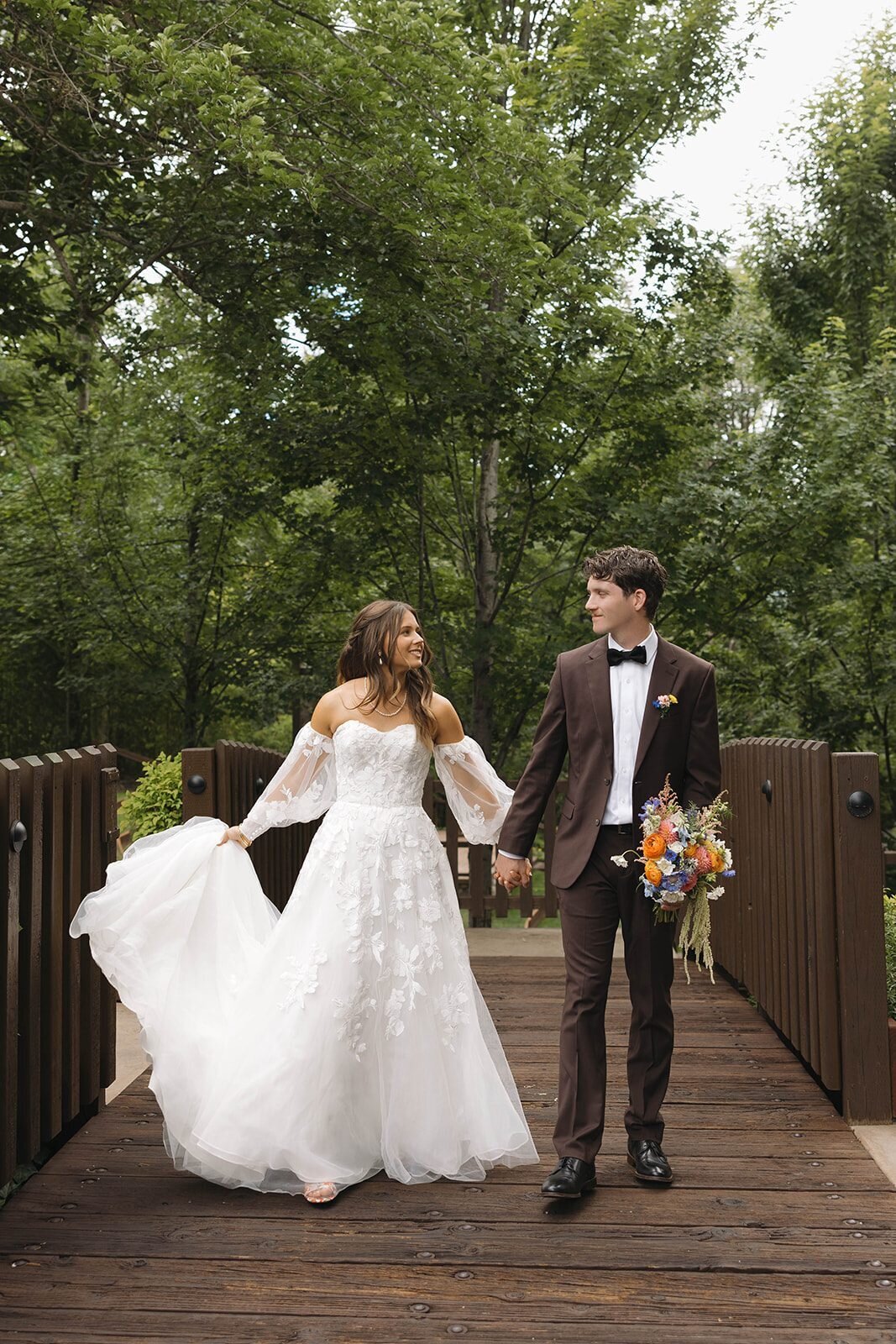 Bride and groom walking hand in hand across a wooden bridge