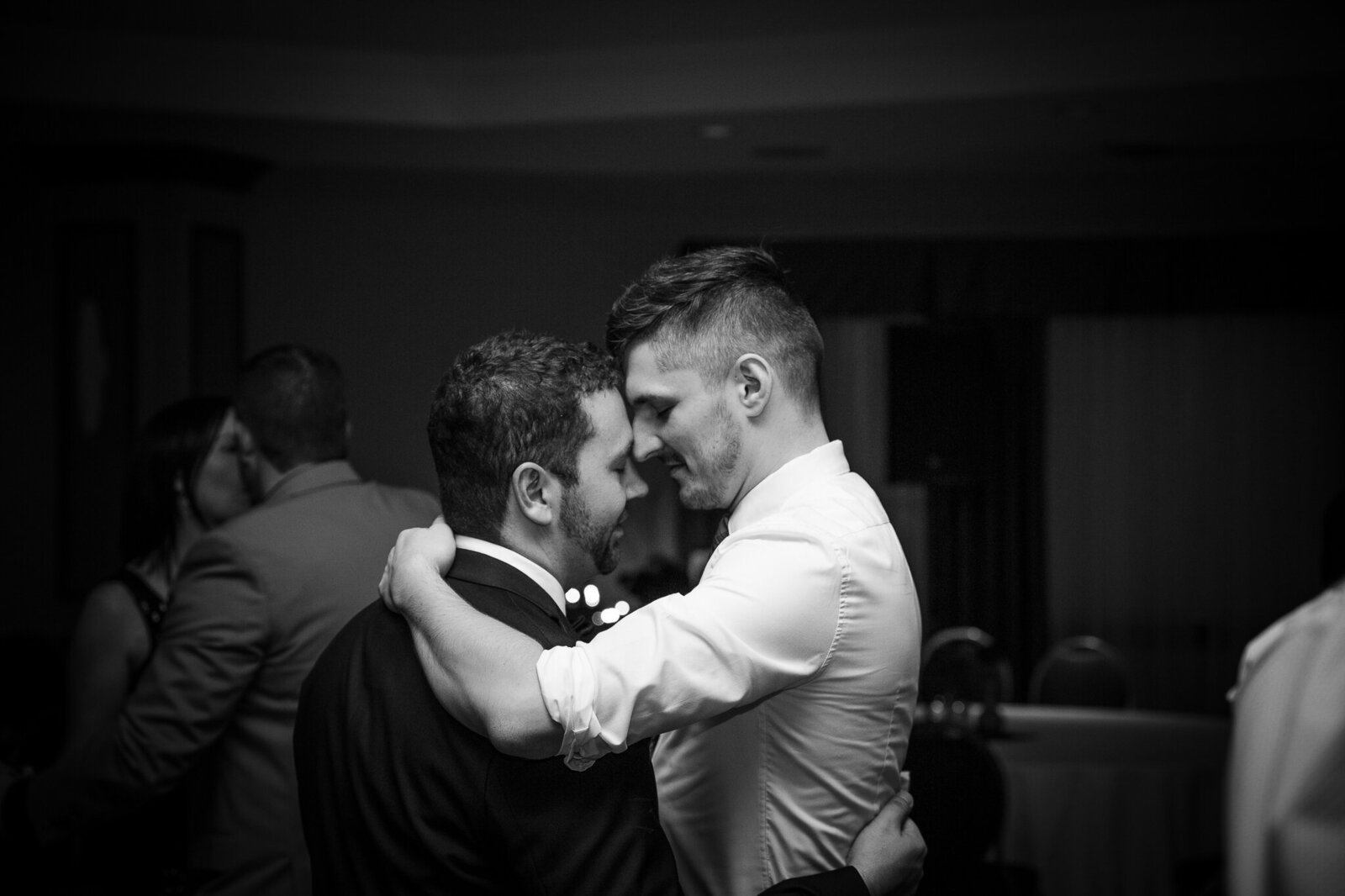 same sex couple embrace during dance at wedding reception.