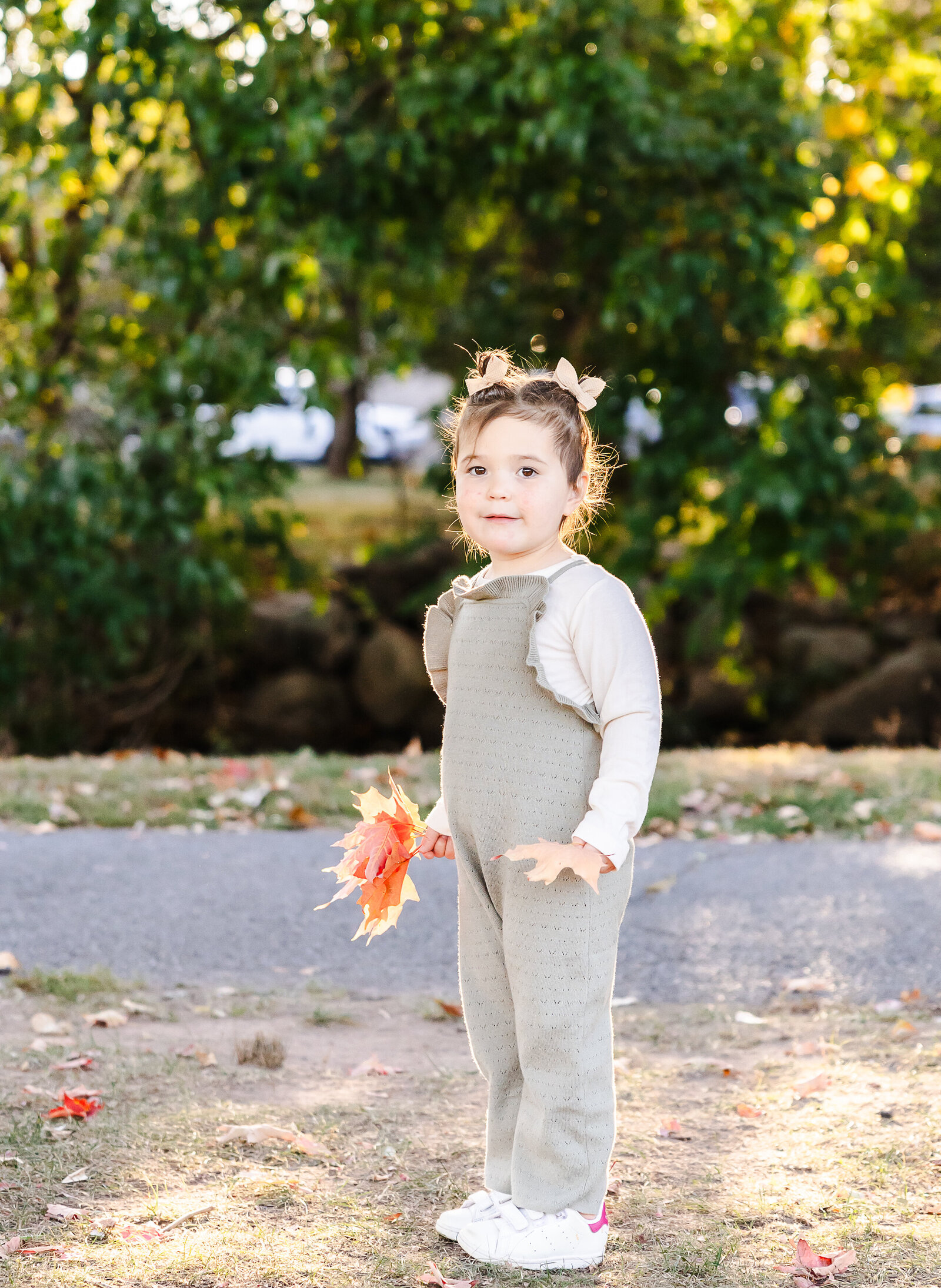 Smiling girl holding an orange maple leaf at an Essex County, New Jersey park in the fall.