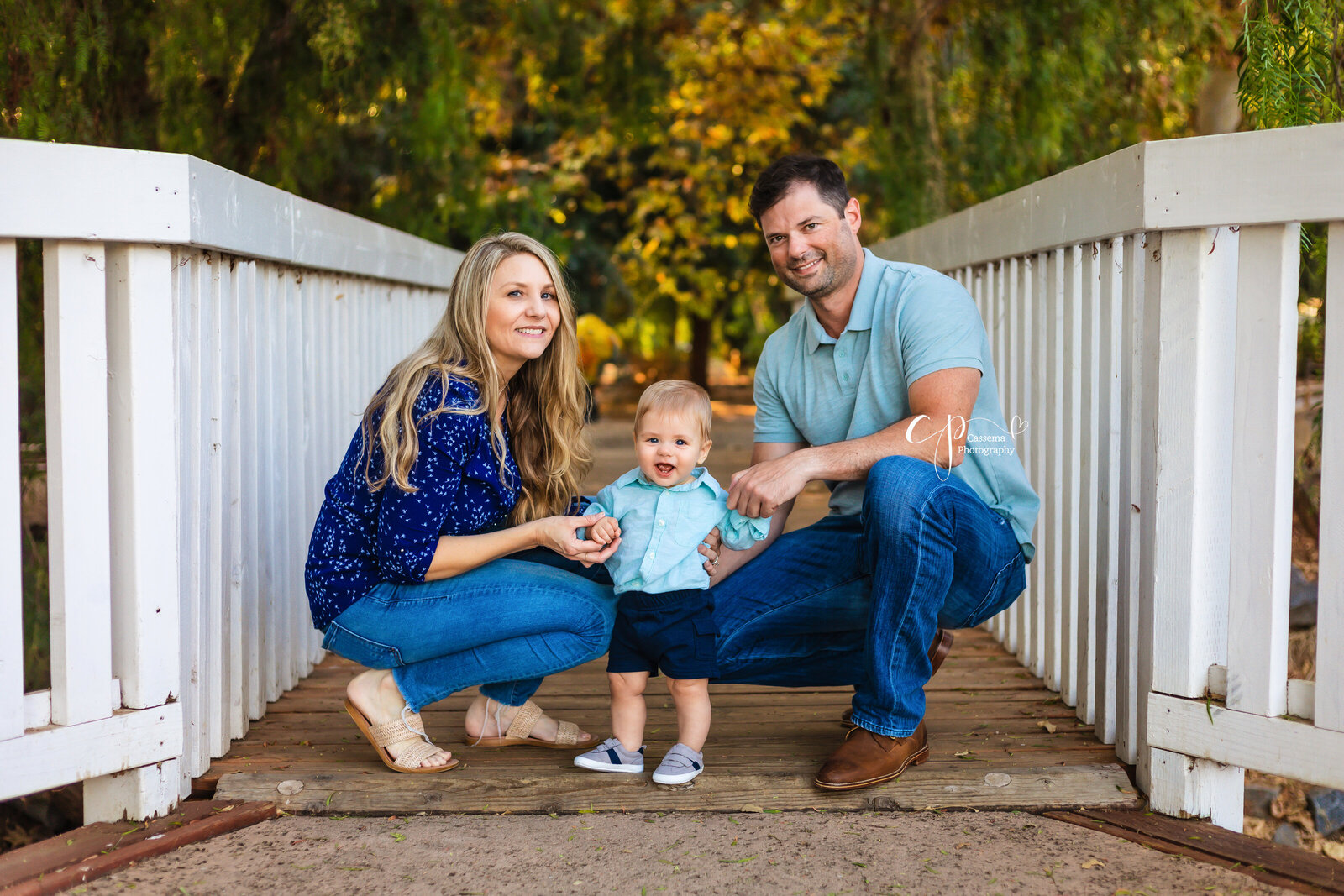 Family Photographer, a young mother and father kneel beside their young boy on a bridge