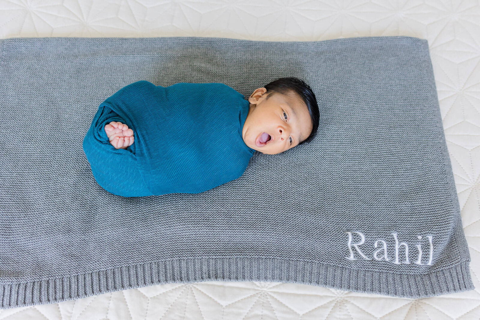 A newborn boy wrapped in teal on a gray blanket.