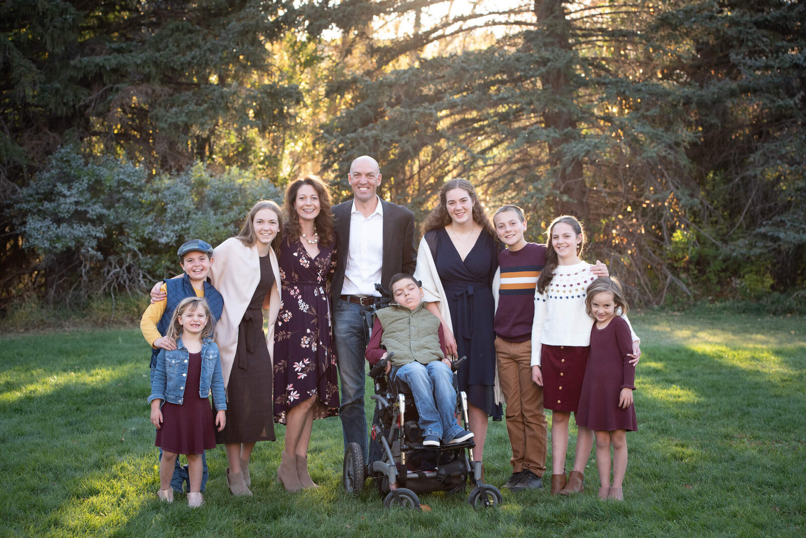 An image from a Denver family photographer of a large family of 10 standing in a park lawn at sunset
