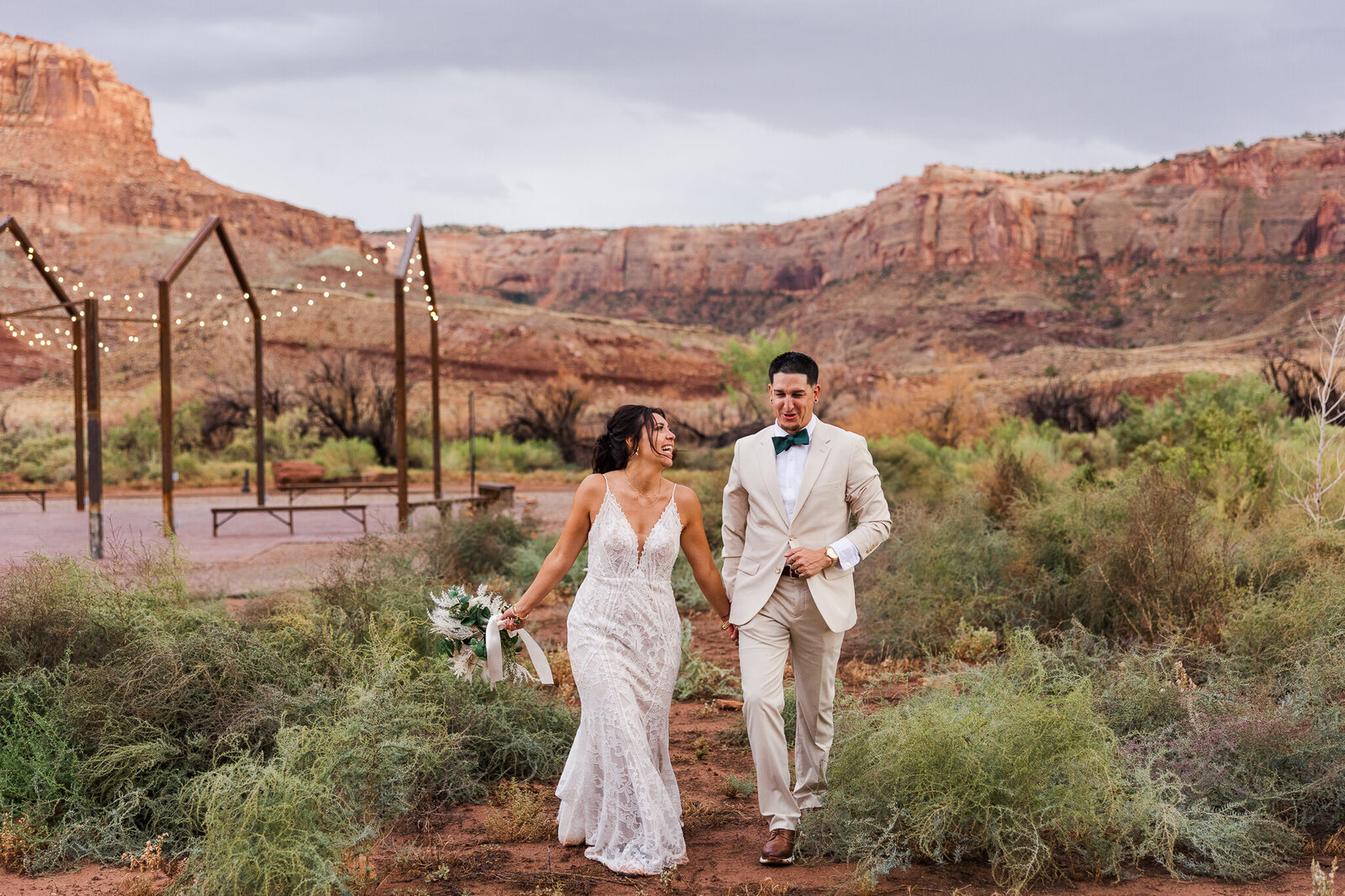 Bride and groom walking towards camera with red earth venue mountains in the background
