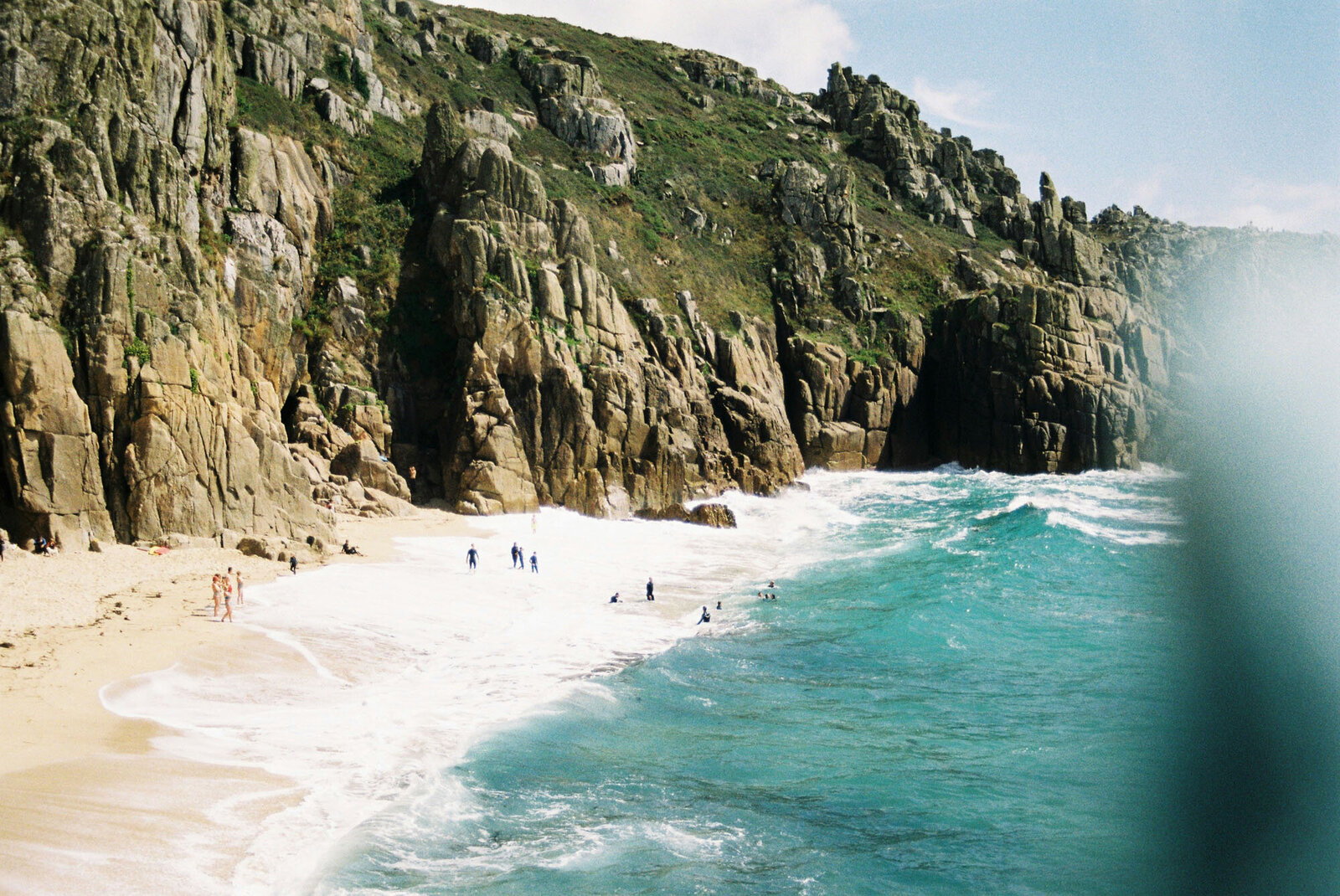 Group of people standing on a beach near a rocky cliff