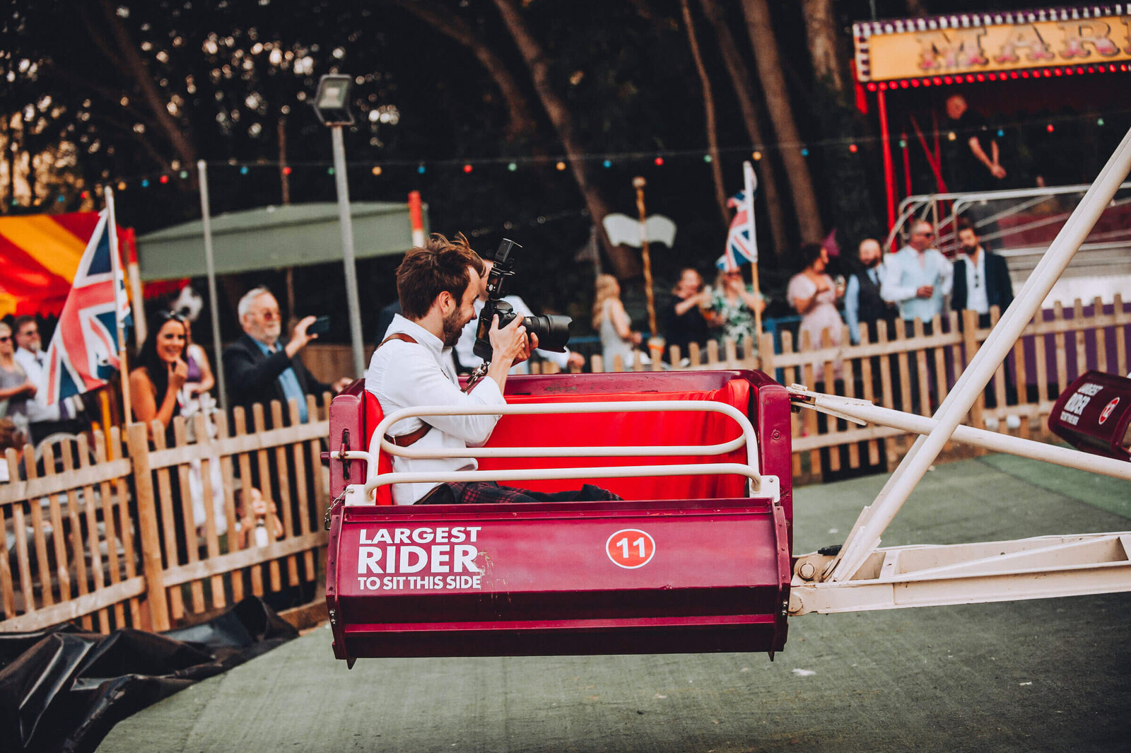 Tom Keenan taking photos from a moving fairground ride, holding his camera with guests celebrating in the background