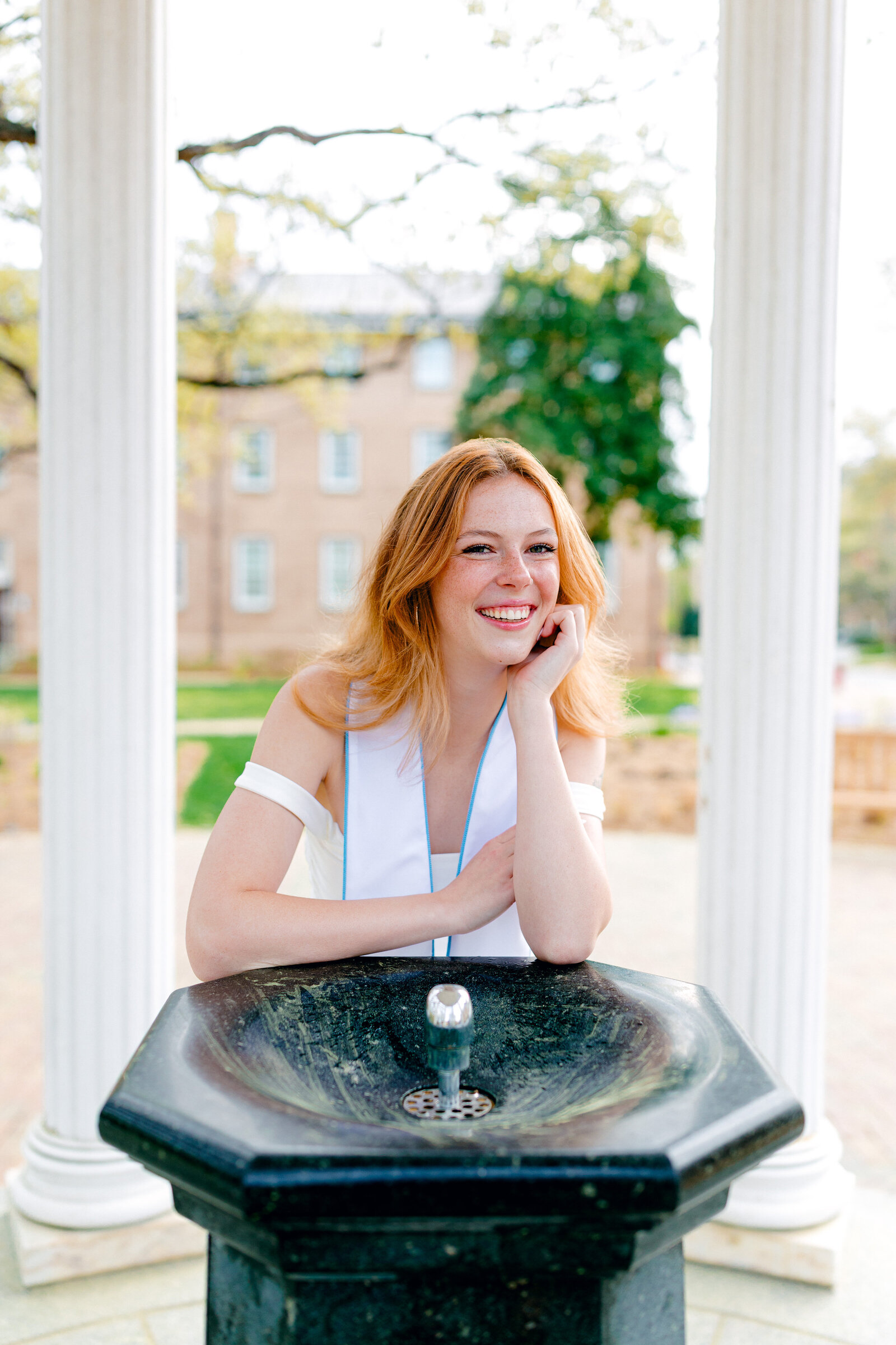 UNC graduate smiling in front of the fountain at the Old Well in Chapel Hill during graduation portraits.