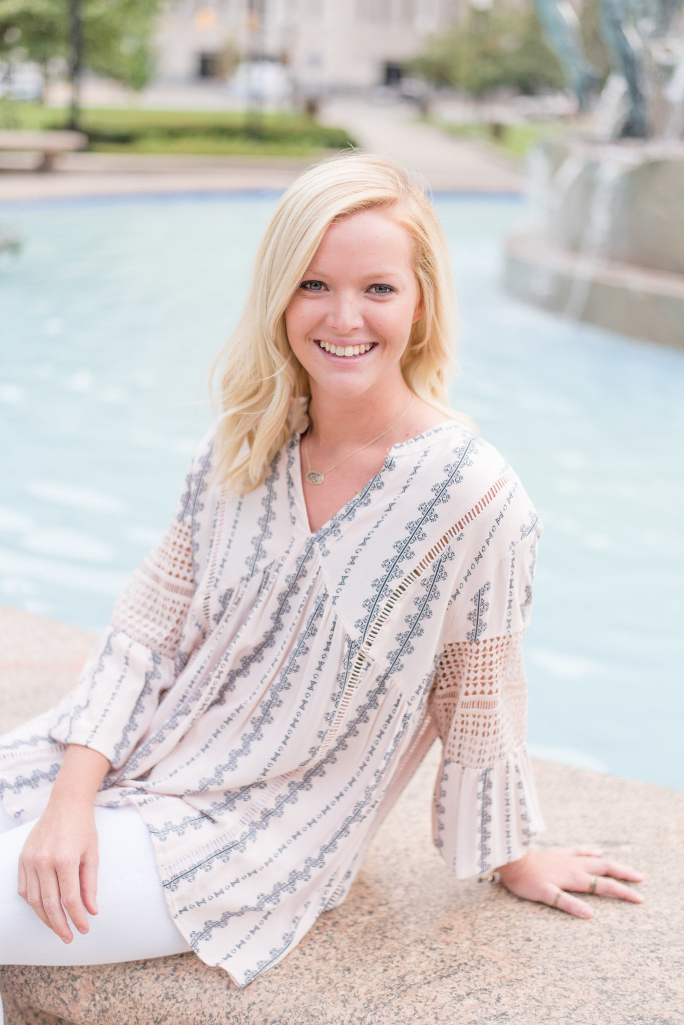 Senior girl sits on fountain and smiles