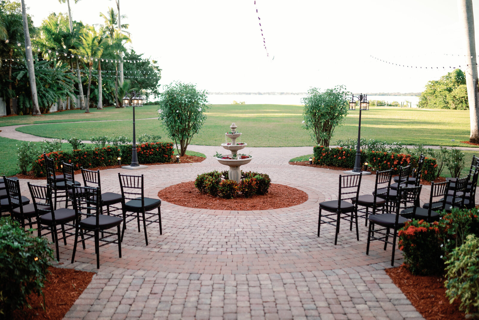 Wedding ceremony site set up in a semi-circle around a small fountain. Black chairs sitting on brick paver stones