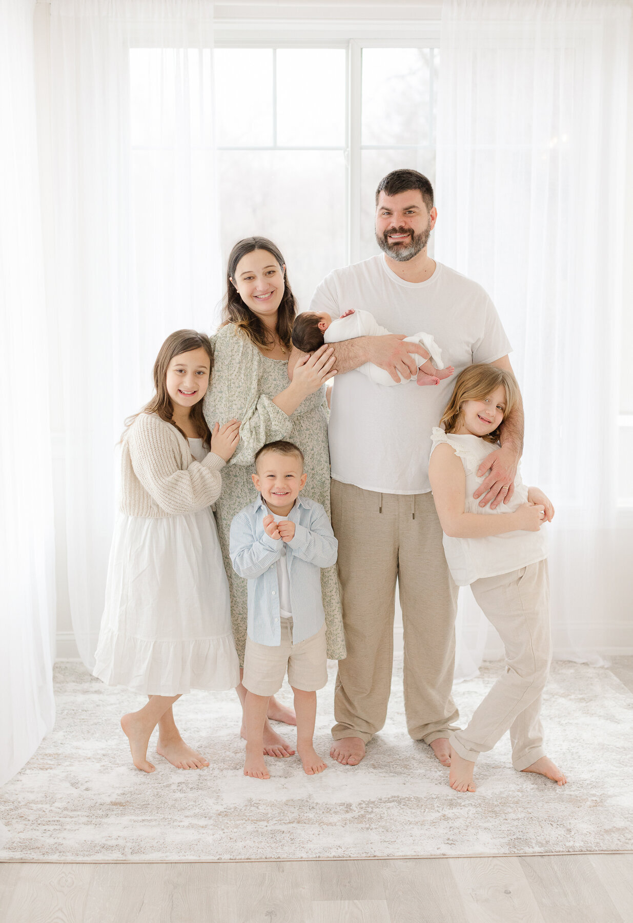 family of six smiles at the camera  during newborn photoshoot in a studio