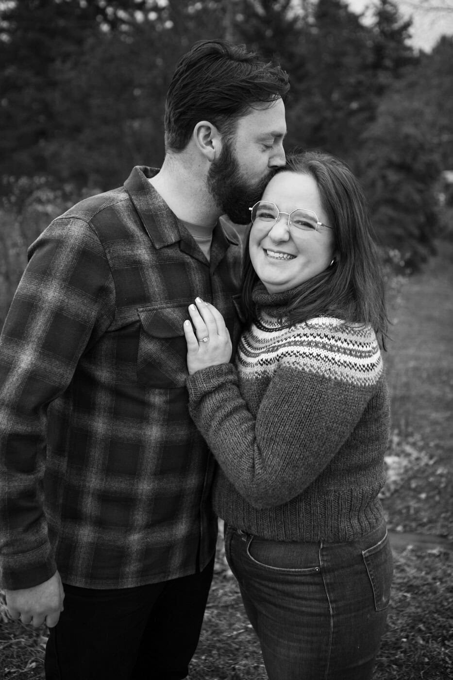 A man kisses a woman's head as she places her left hand on his chest.