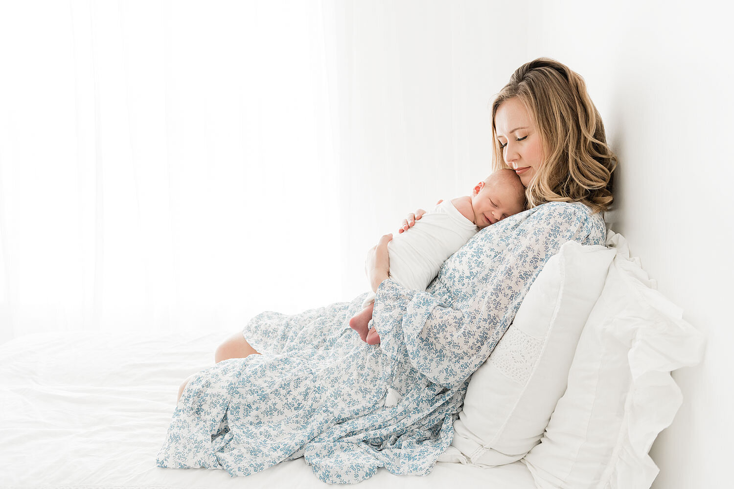 pretty mother snuggling her newborn son on a bed while being photographed by Andrea Krey Photography