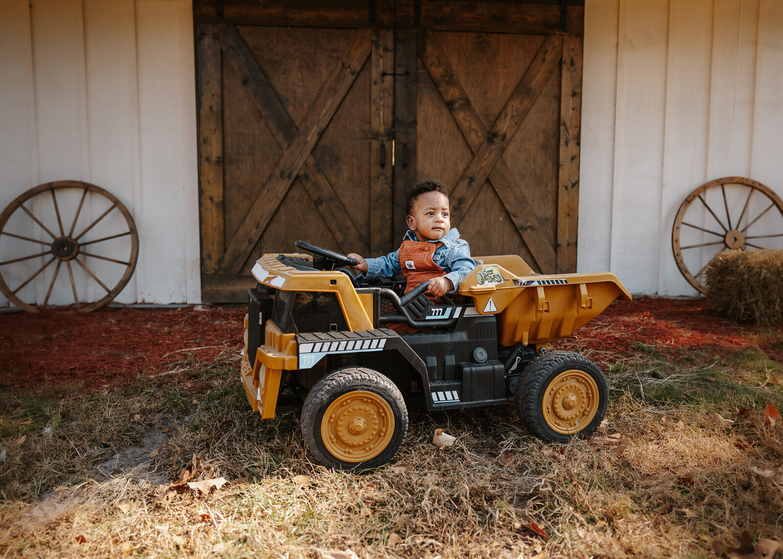 Baby boy sitting in a toy tractor during his 6-month milestone photoshoot in Aiken SC, in front of rustic barn doors.