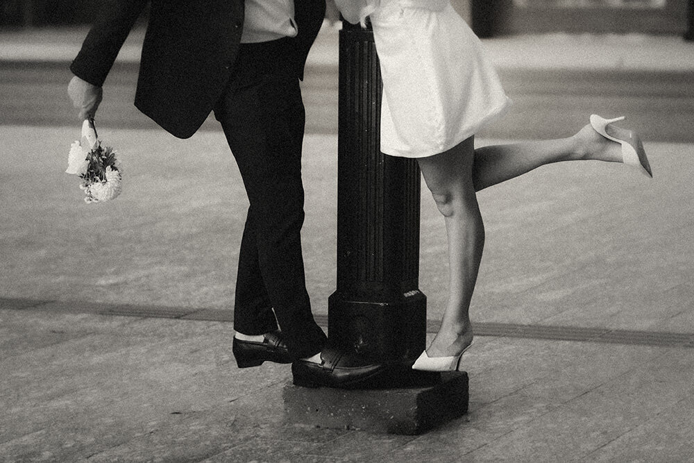 Black and white image of the legs of a bride and groom eloping with a lamppost and a bouquet