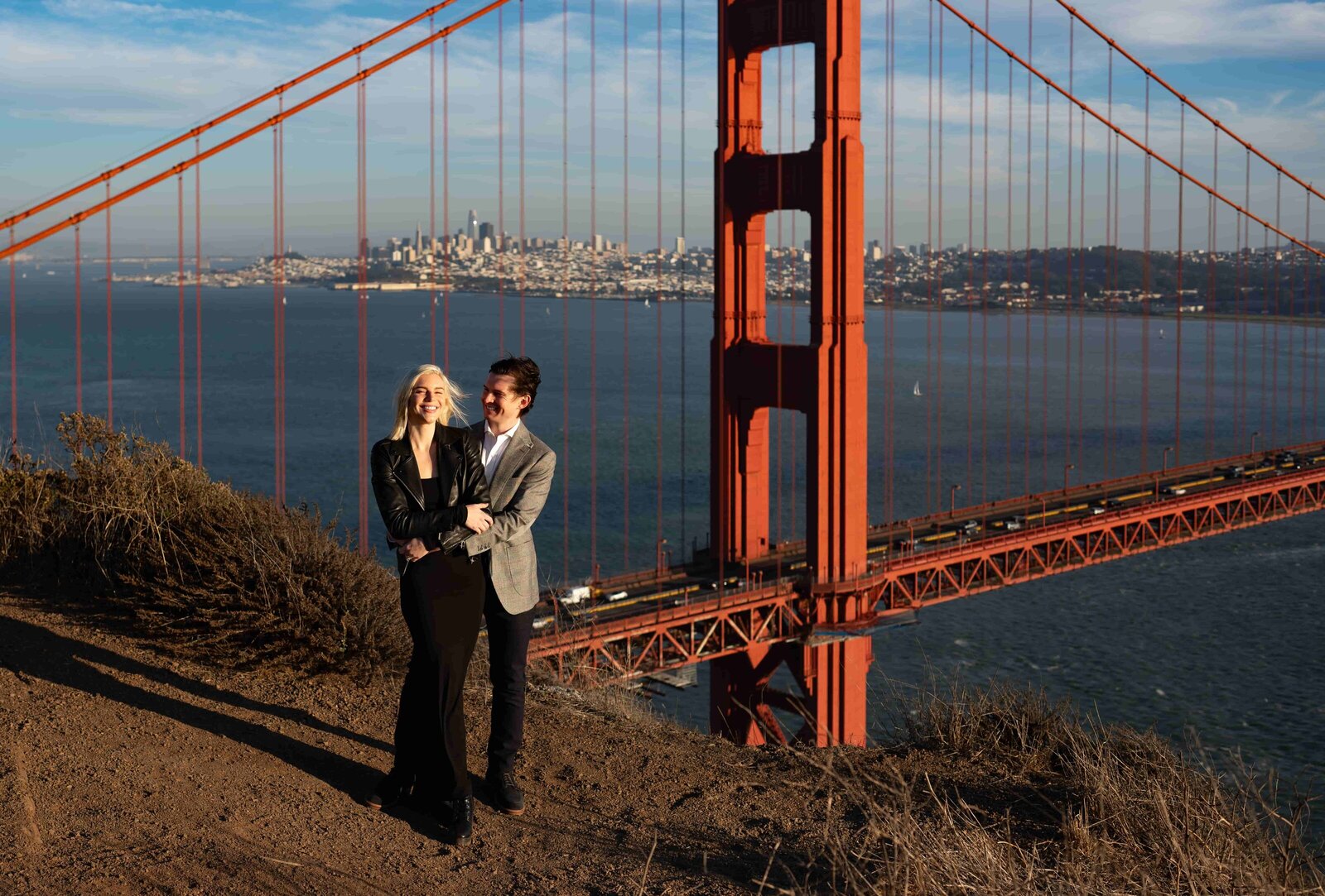 Smiling couple embracing on a cliff overlooking the golden gate bridge during golden hour a sunset