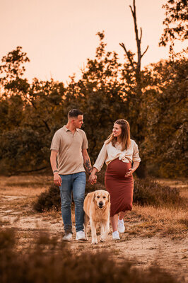 Een aanstaande moeder en haar partner poseren liefdevol met hun hond tijdens een zwangerschapsshoot, een intiem moment vol warmte en verwachting