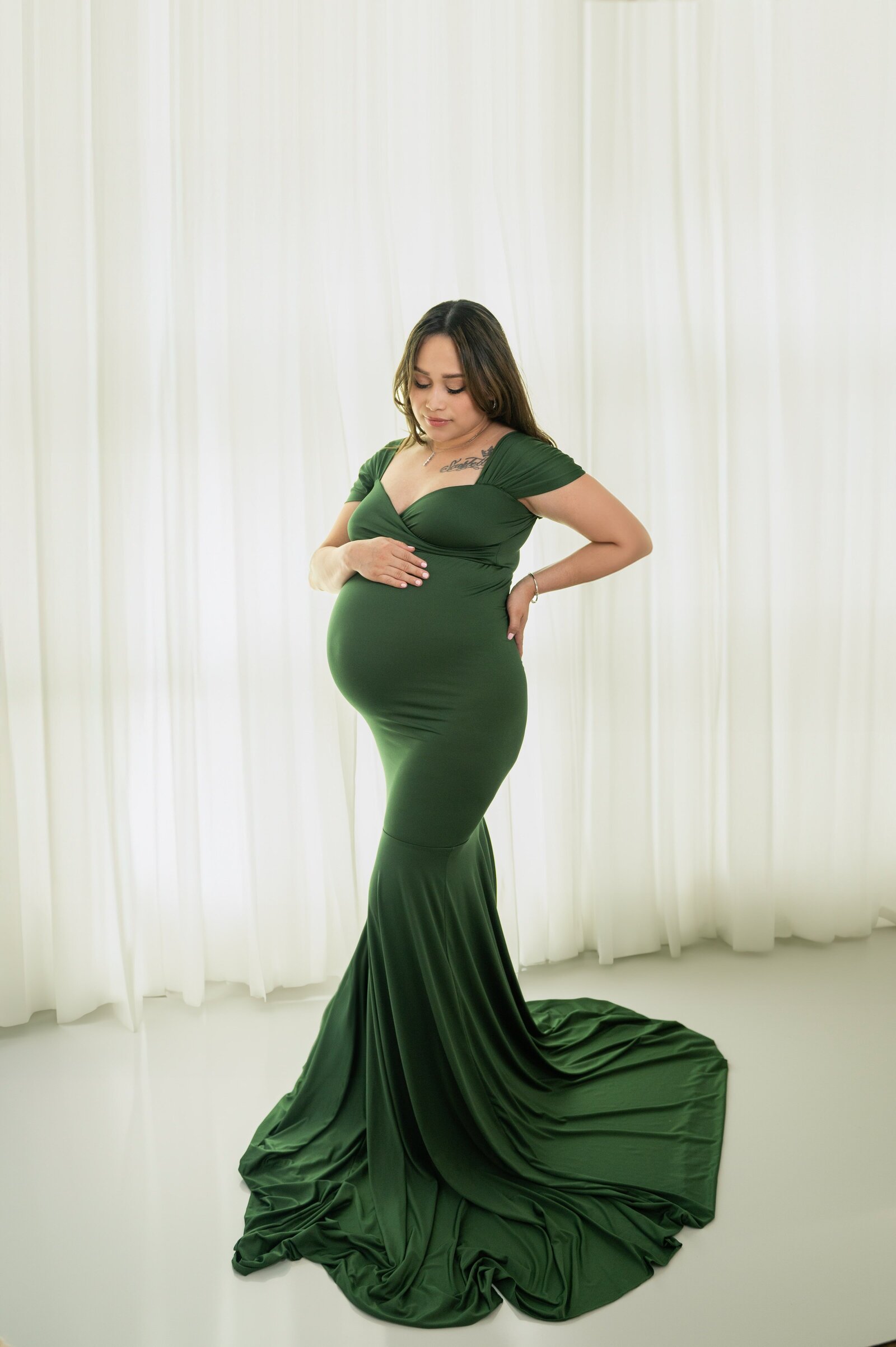 woman holding pregnant belly in a fitted emerlad green dress