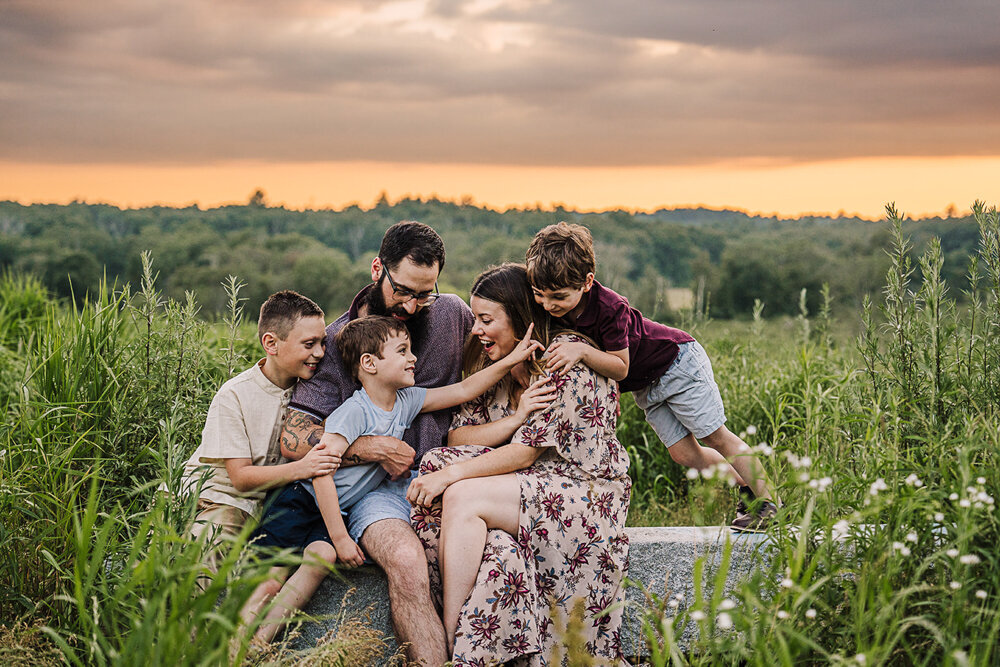 family with three boys sits in grassy field for boston photo session