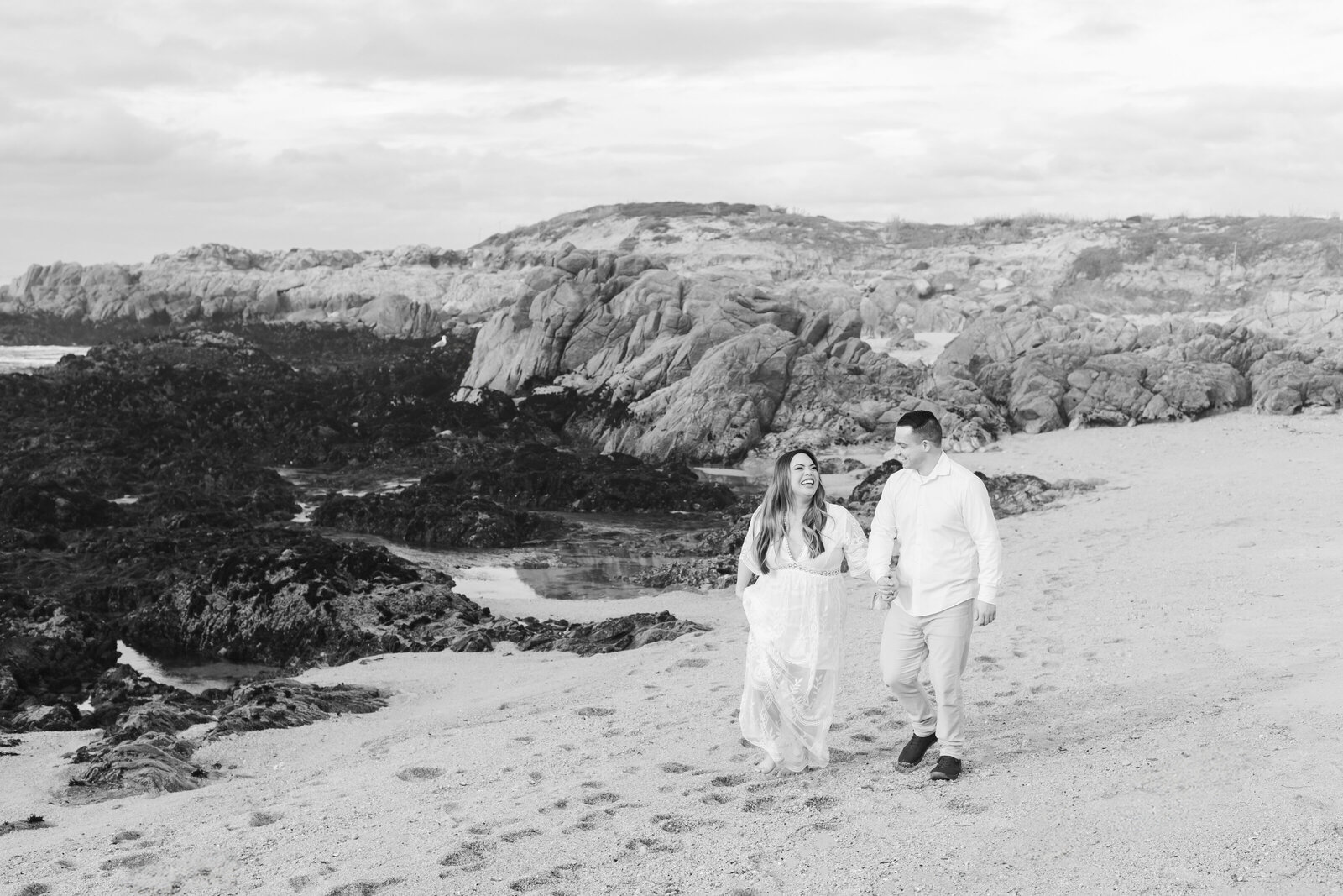An engaged man and woman take photos on the beach in Pacific Grove, Monterey, California near Big Sur.