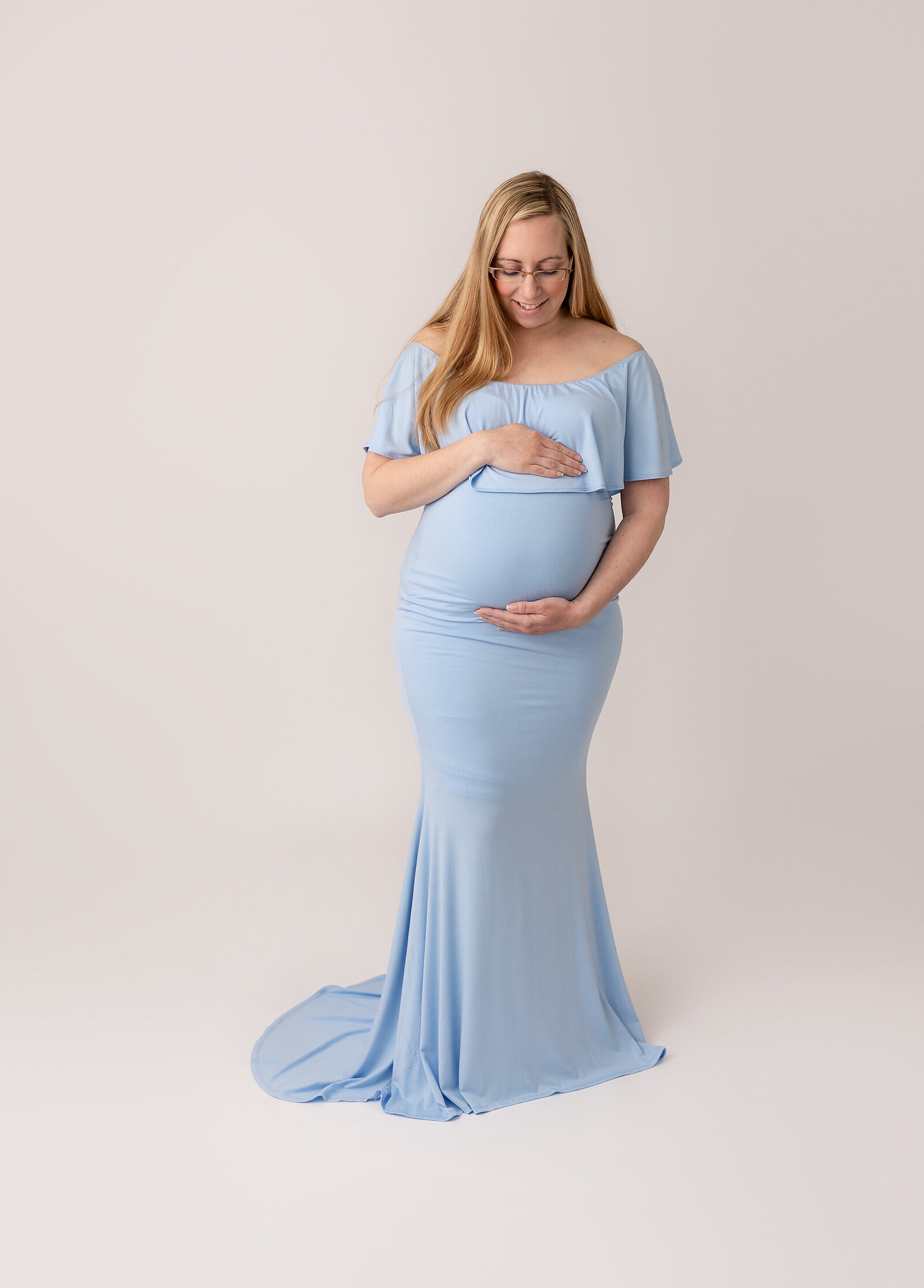 pregnant woman in blue dress holding baby belly in studio