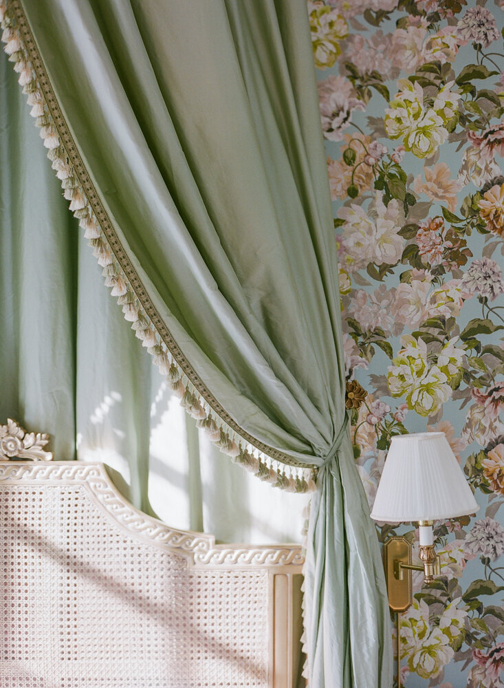 sage green satin drapes framing a natural rattan bed and wall mounted lamp
