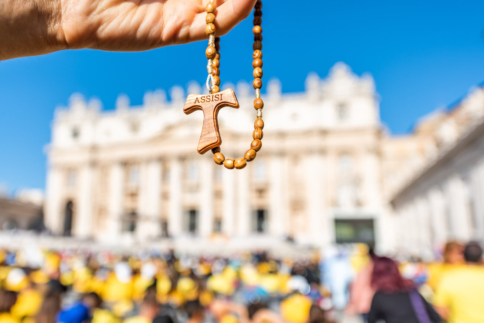 Macro closeup of wooden handmade Italian cross Catholic Assisi rosary with bokeh background of Vatican church St Peter's Square Basilica