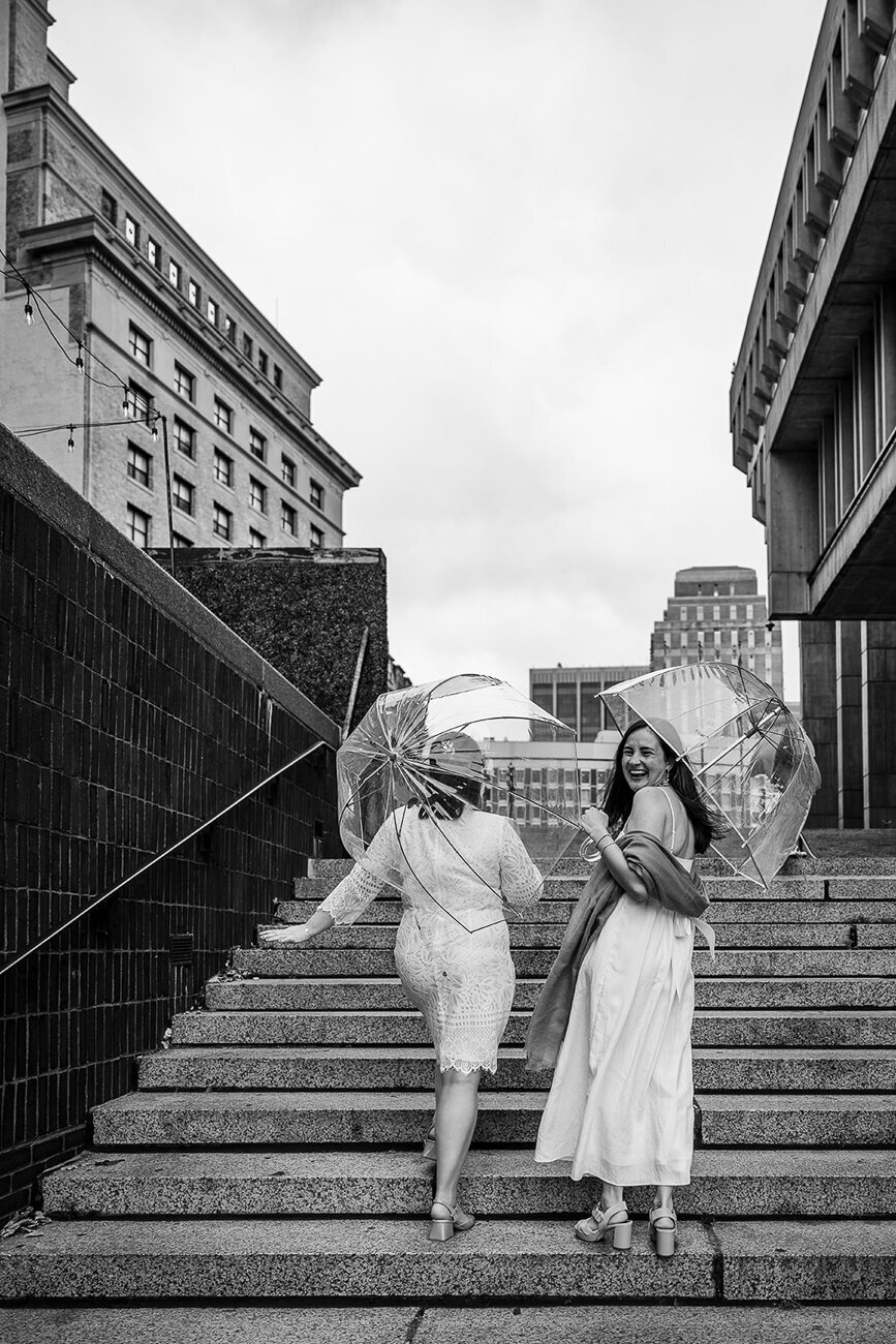 two brides smile and laugh at the camera on the steps at boston city hall