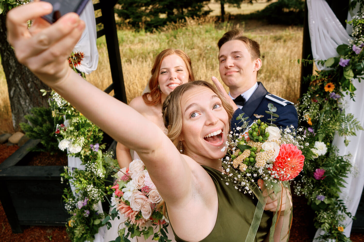 Bridesmaid holds her phone up to take a selfie with the bride and groom