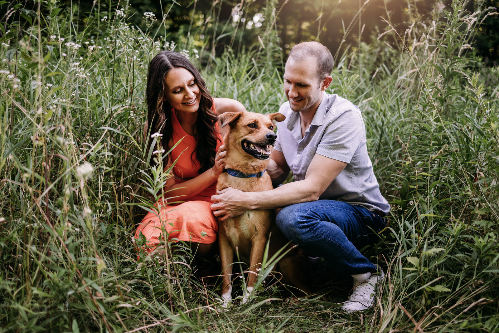 Sweet couple showing their family dog affection amongst tall grass