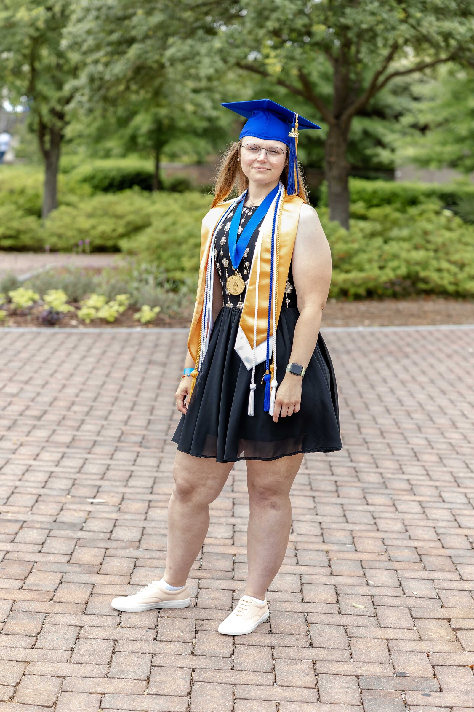 A senior in a blue cap and gown adorned with honor cords, posing confidently on a brick path at CFCC in Wilmington, North Carolina. This photo exemplifies the celebration of academic success, ideal for those seeking professional graduation photography.