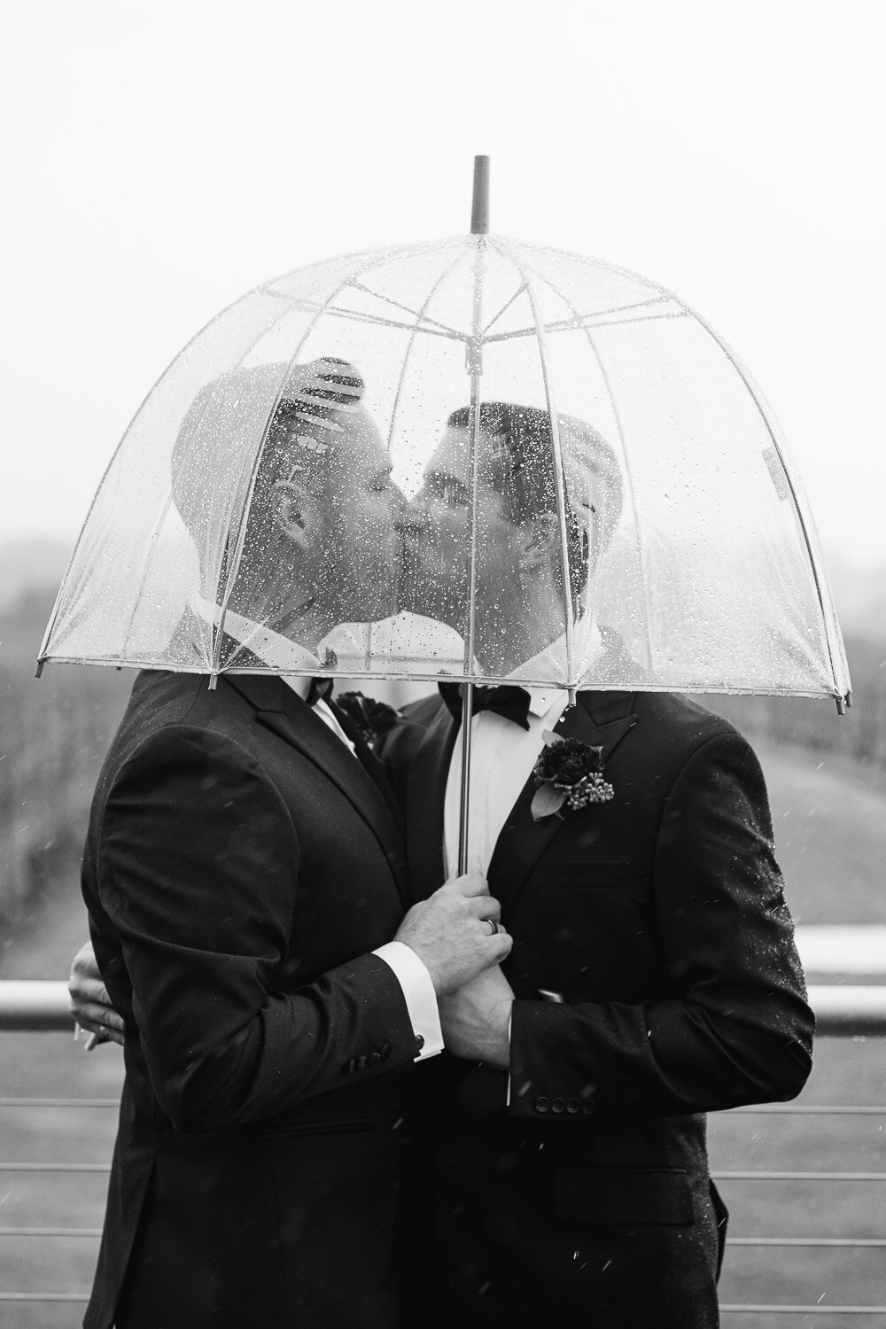 grooms kiss under umbrella in rain