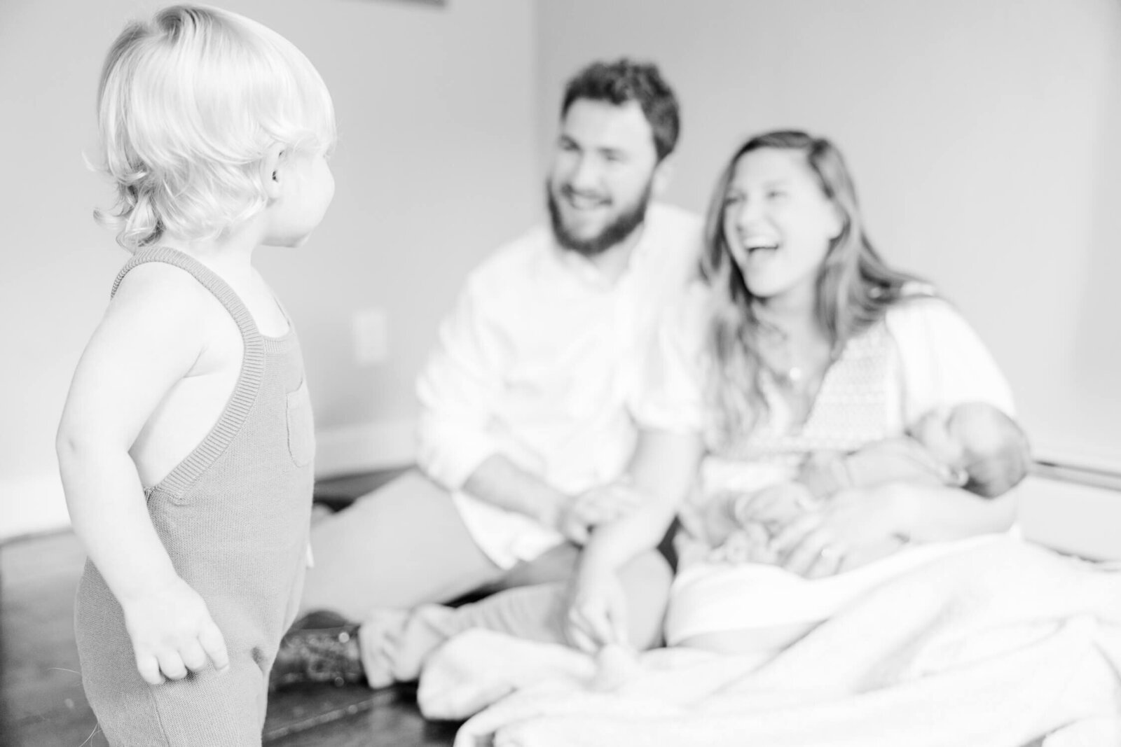 Toddler looks at his laughing mom and dad, black and white