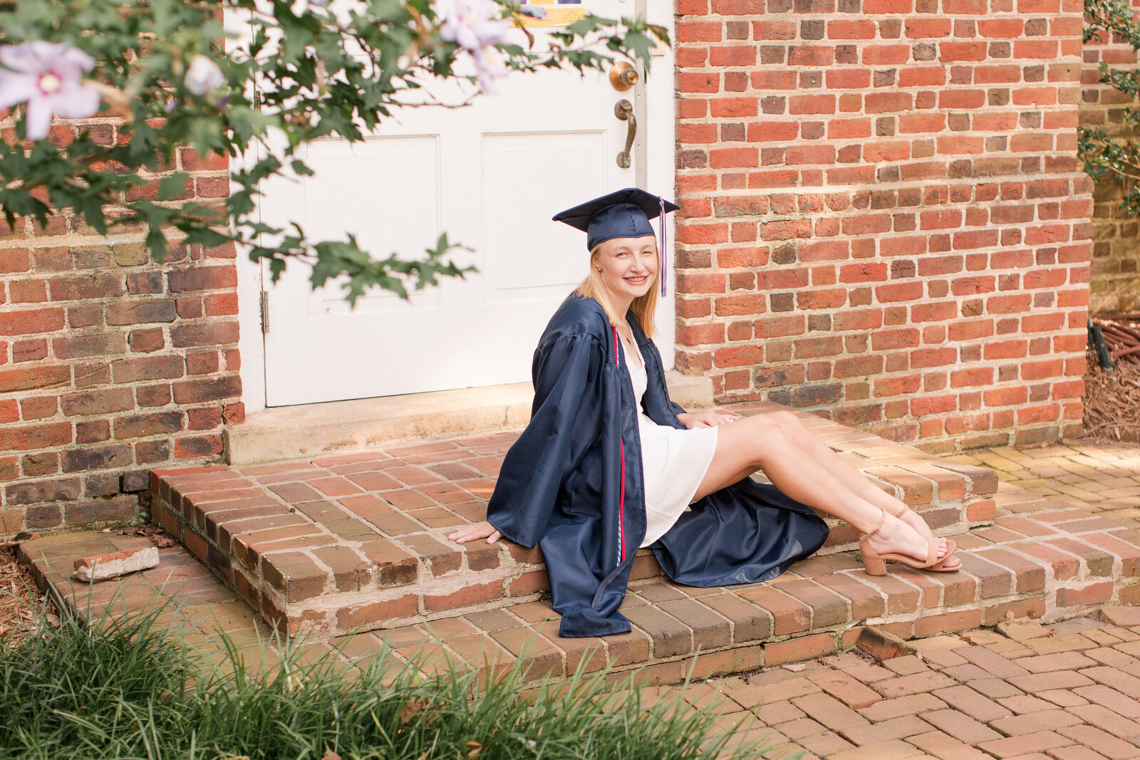 senior girl in cap and gown on a brick step