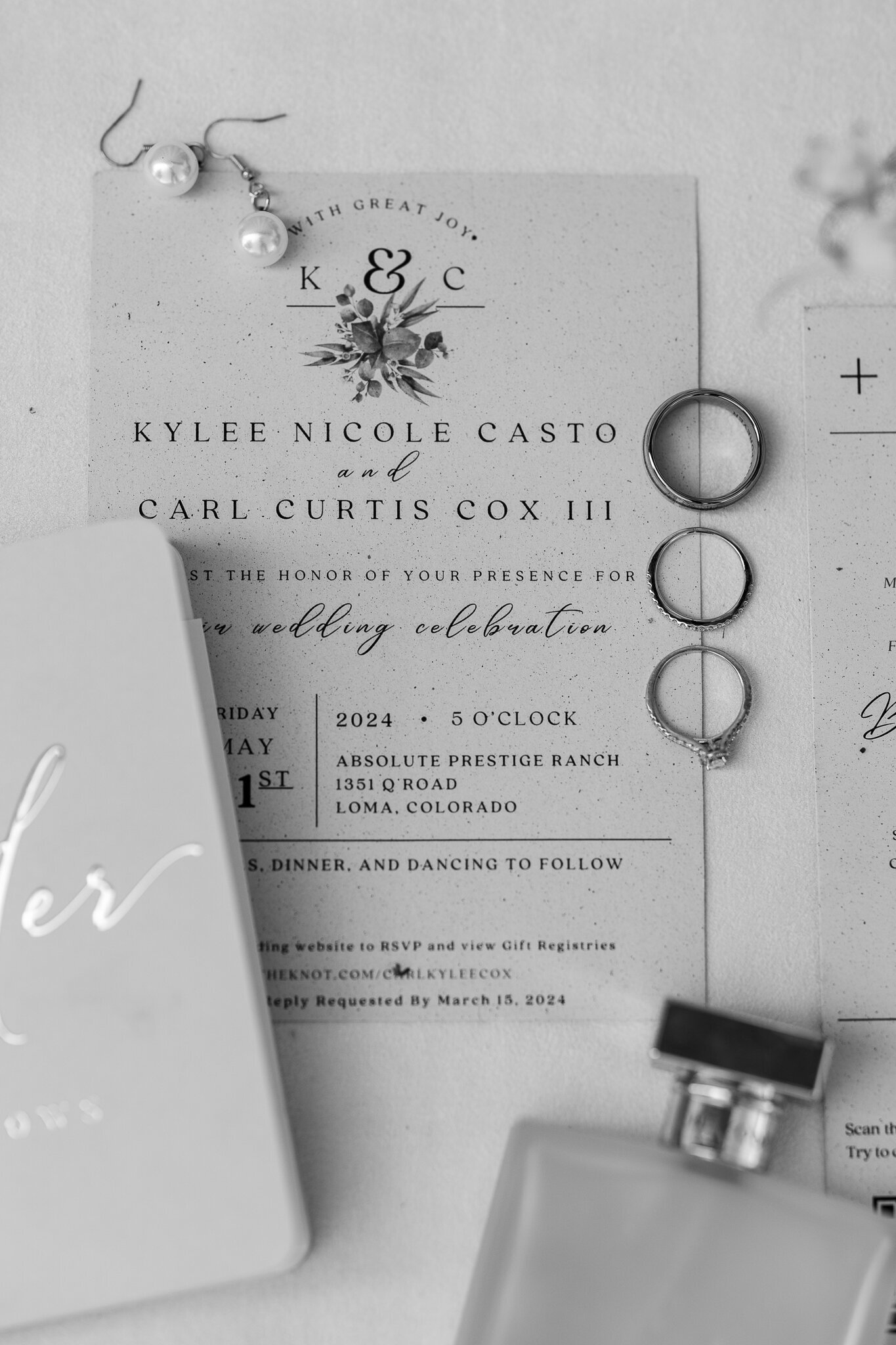Black and white detail image of the wedding invitation and rings at Absolute Prestige wedding venue in Loma, Colorado